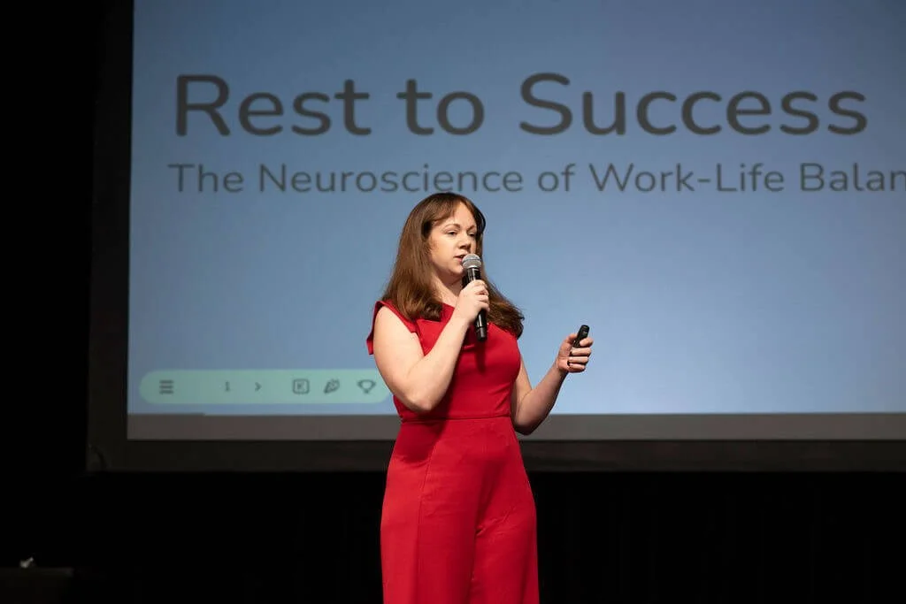 Nina Nesdoly presenting Rest to Success keynote on work life balance neuroscience, speaking on stage with microphone