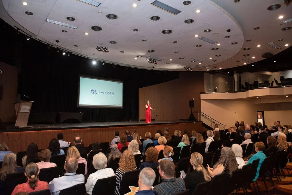 Nina Nesdoly speaking on stage at conference, wide view of audience watching keynote in large auditorium