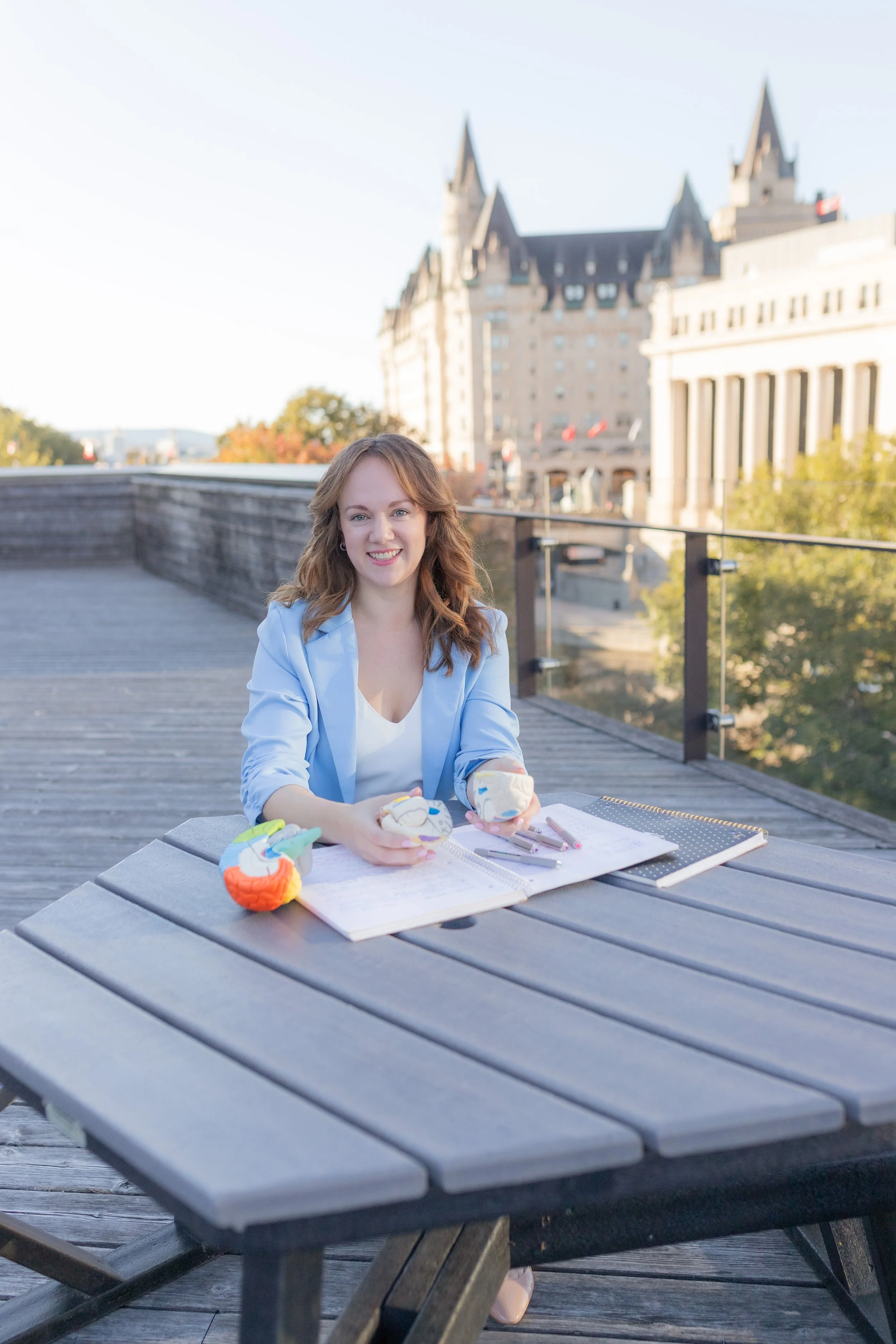 Nina Nesdoly sitting at a table outside with a notebook, holding a model brain