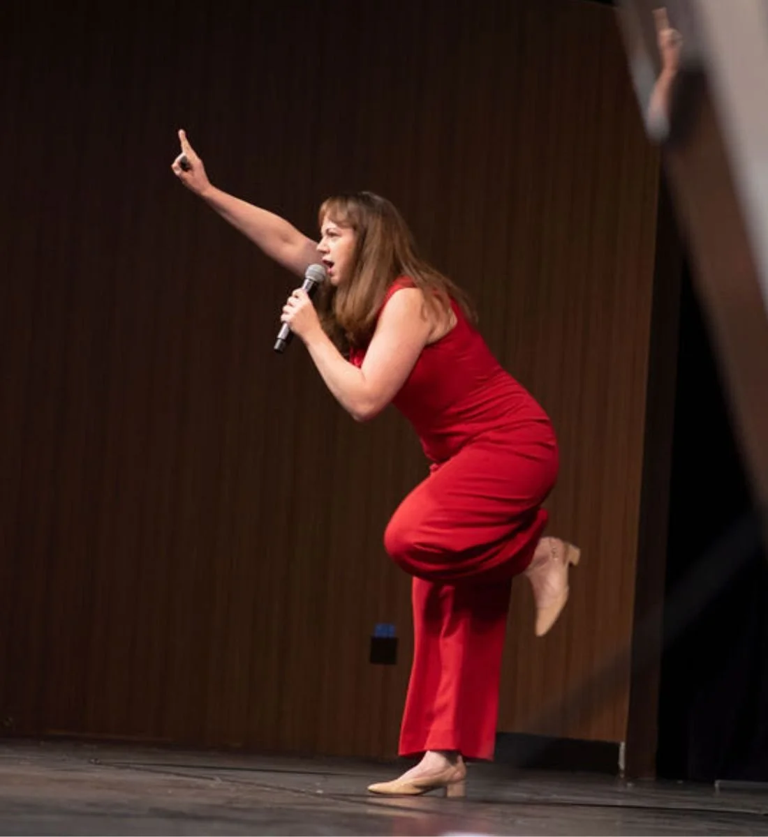 Nina Nesdoly keynote speaker in red outfit presenting energetically on stage, pointing upward during live presentation