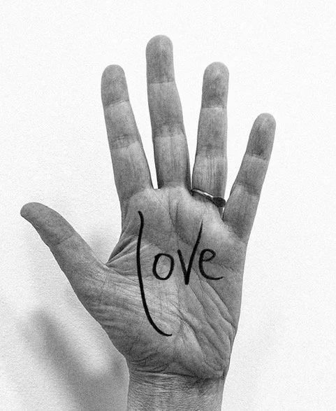 black & white image of a hand, palm facing the viewer, with the word "love" written on the palm