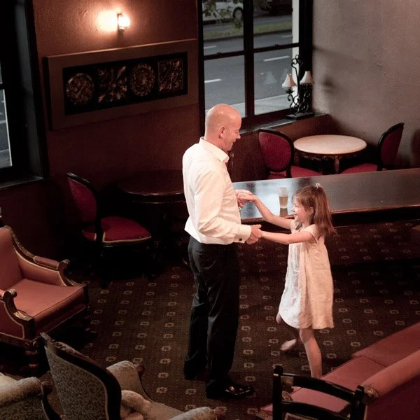 A man and a young girl dancing together in an elegant venue with vintage-style furniture and large windows. Event photography by Natural Family Photography, Melbourne.