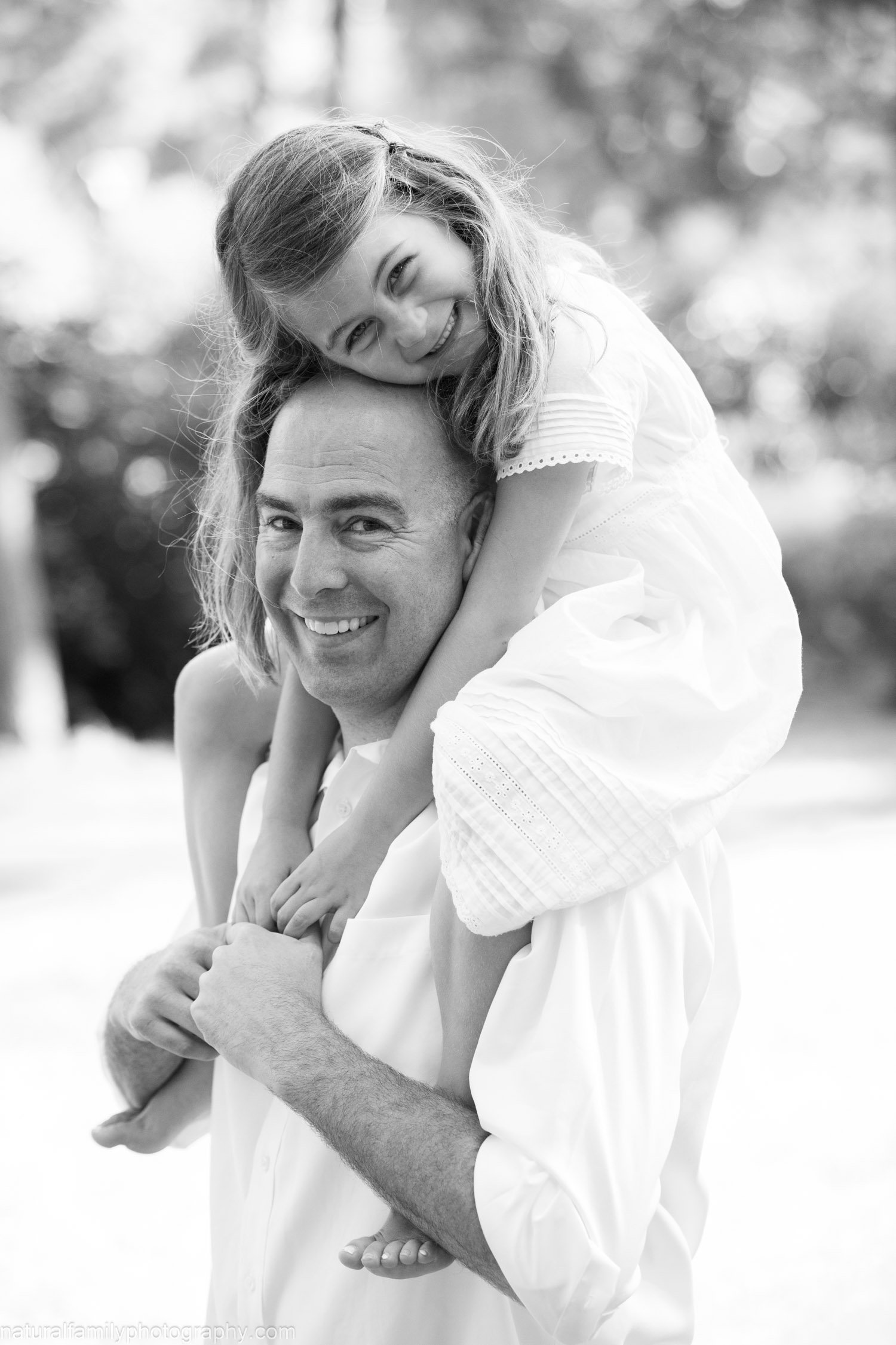 A man carrying a smiling young girl on his shoulders outdoors.