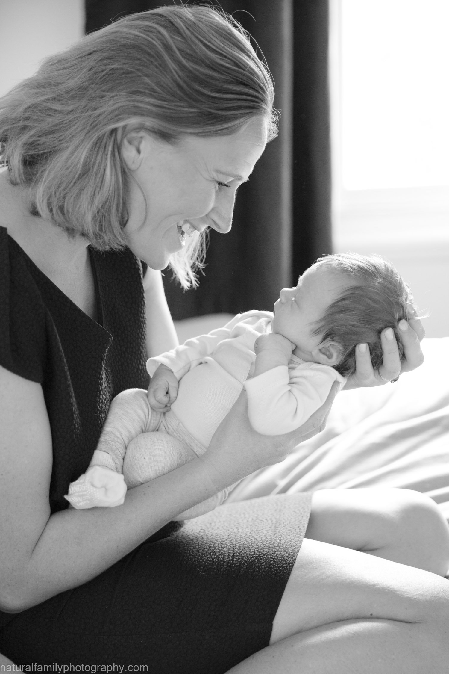Woman holding a newborn baby and smiling at each other in black-and-white photograph.