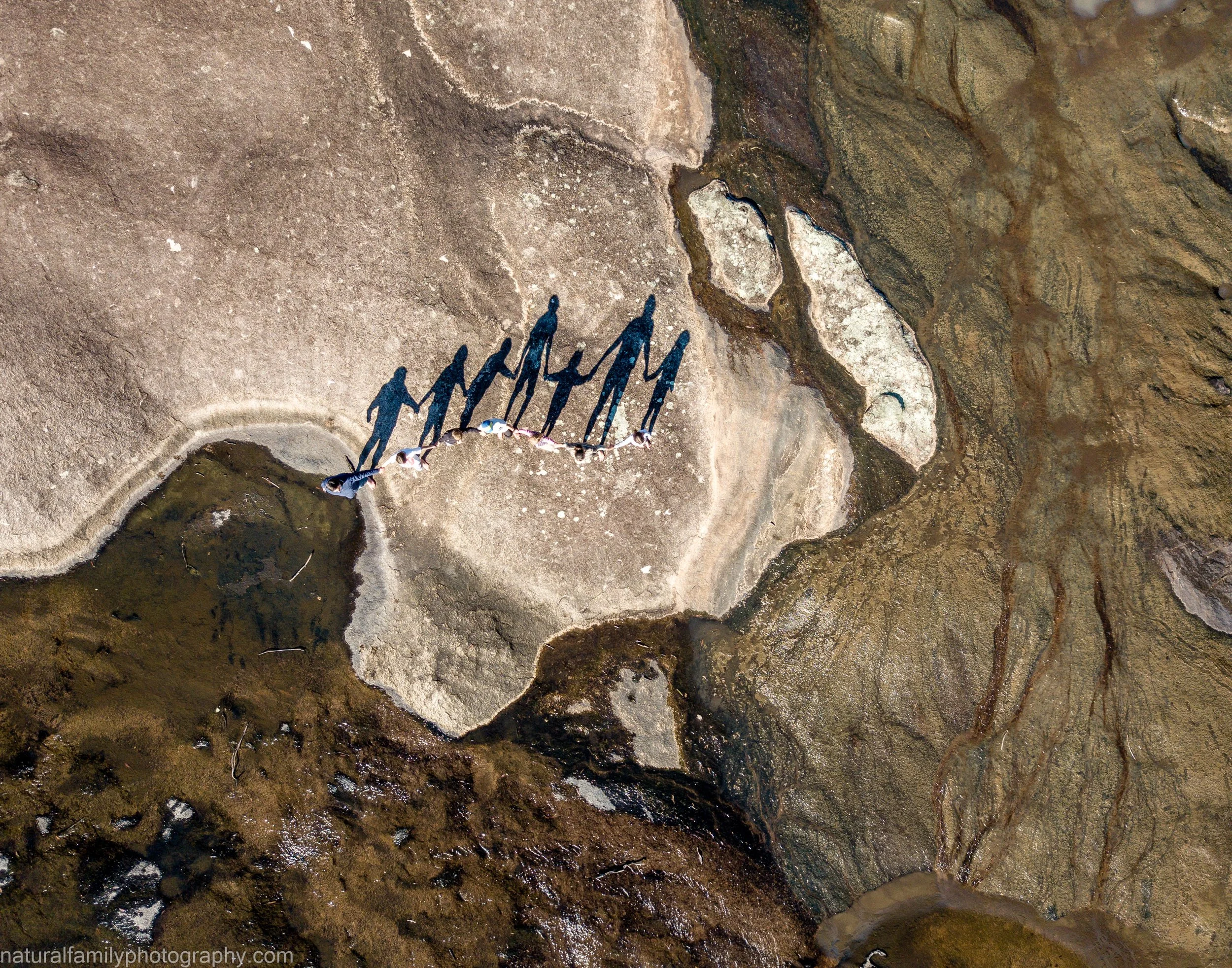 Aerial view of a family of seven standing across a large, rocky area casting long shadows on the ground.