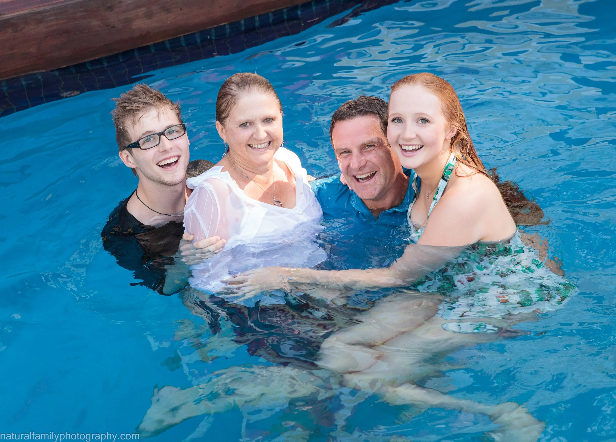 A family swimming together in a pool, smiling and enjoying their time.