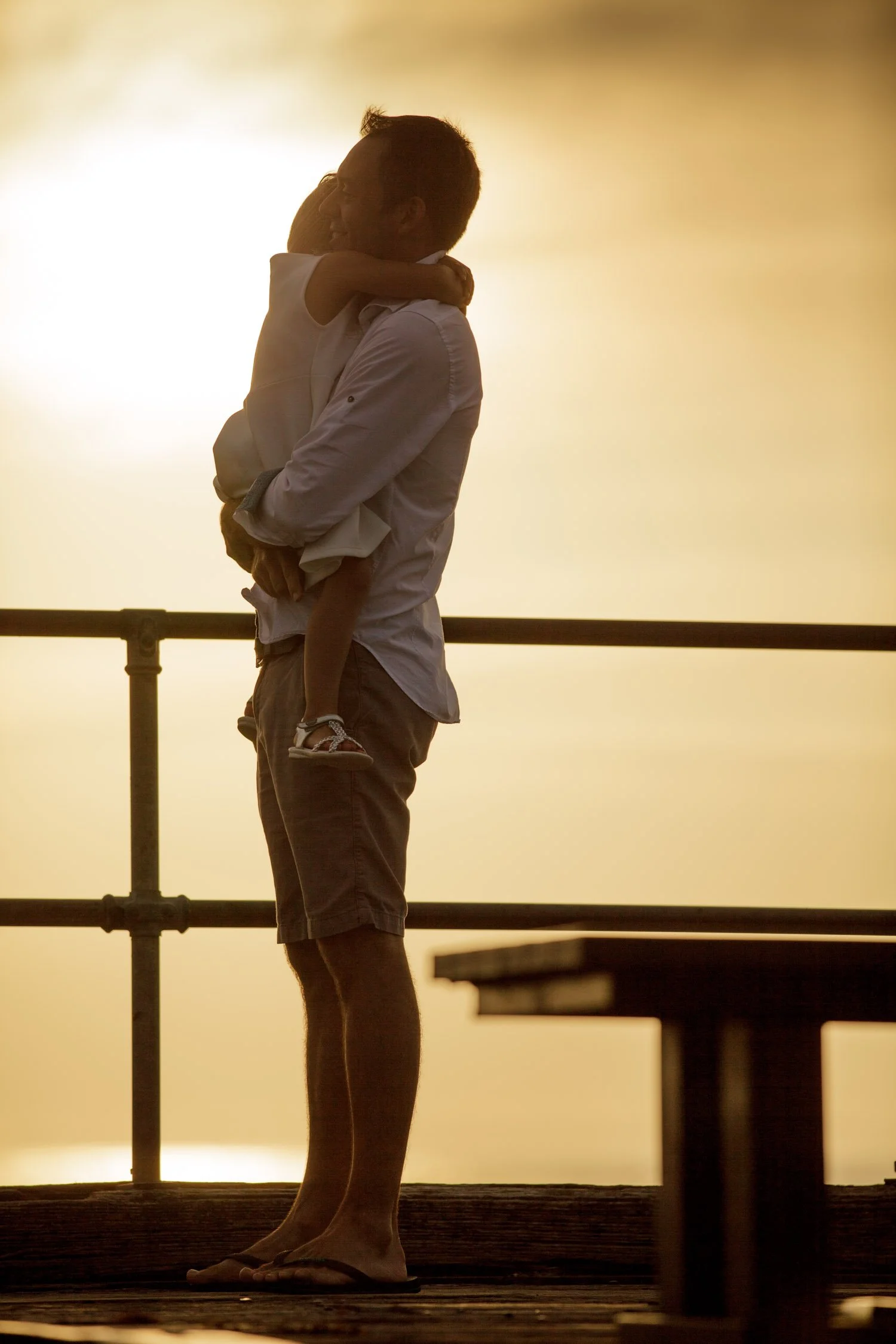 A man holding a young girl as they hug each other with the sunset in the background.