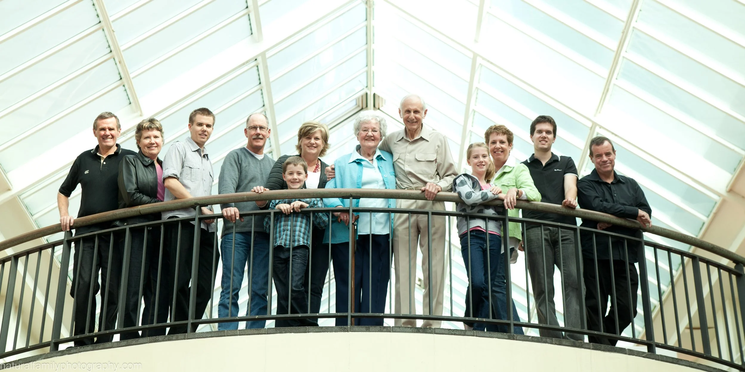 Group of people smiling on a balcony inside a building with glass ceiling.