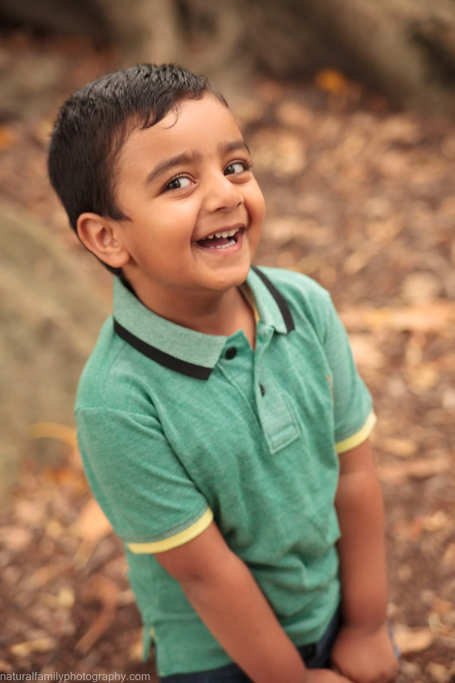 A smiling boy with short dark hair wearing a green polo shirt outdoors.