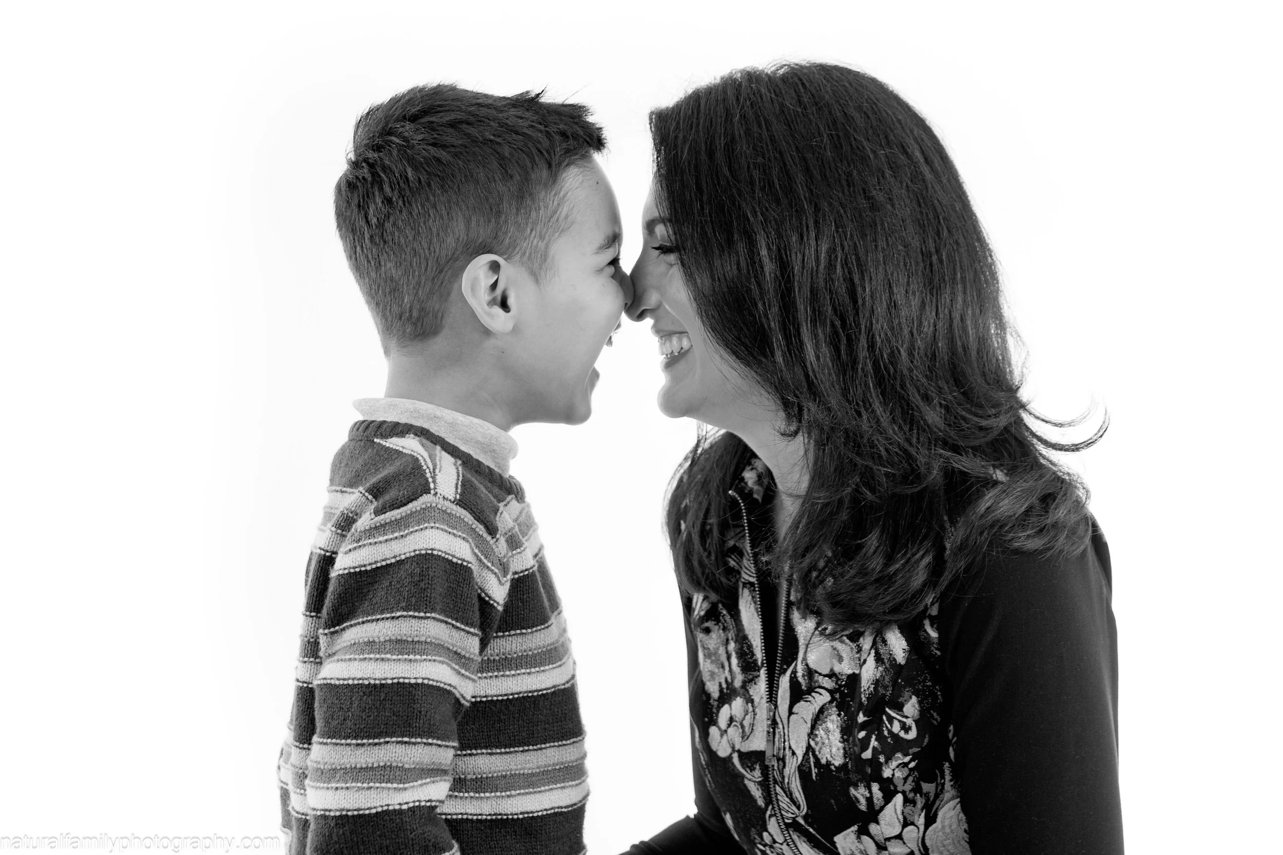 A boy and a woman with their noses touching, smiling at each other, in a black and white photo.