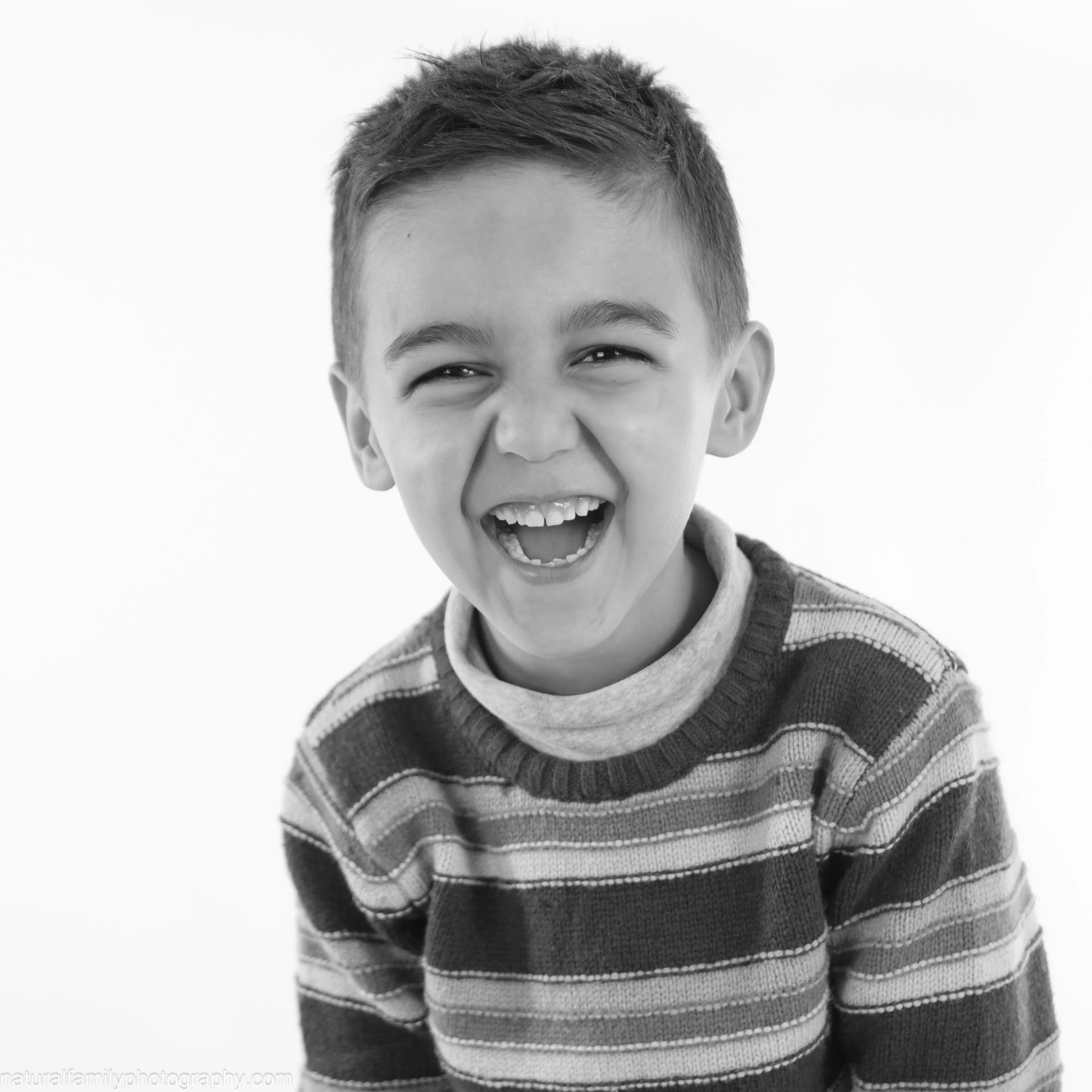 A young boy with short hair laughing joyfully, wearing a striped sweater.