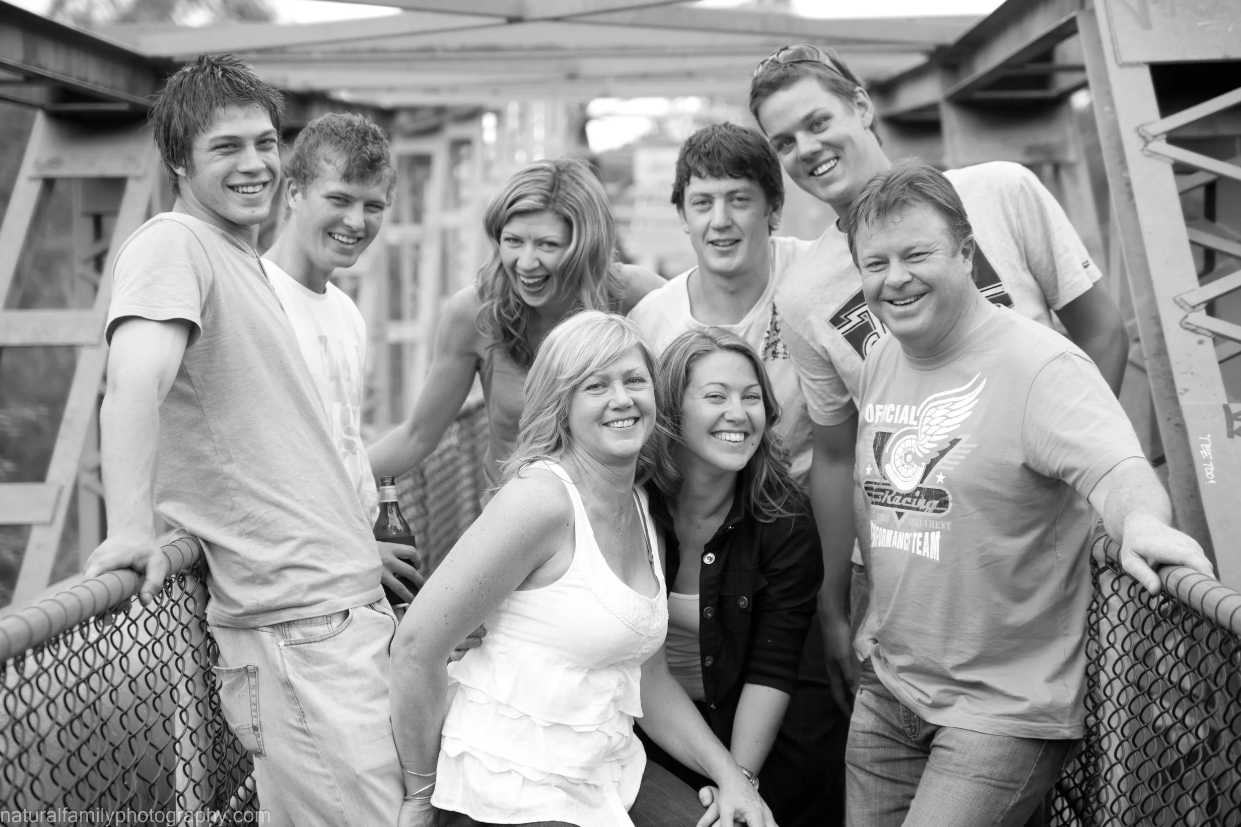 Group of nine people smiling and posing together on a bridge under construction, in black and white.