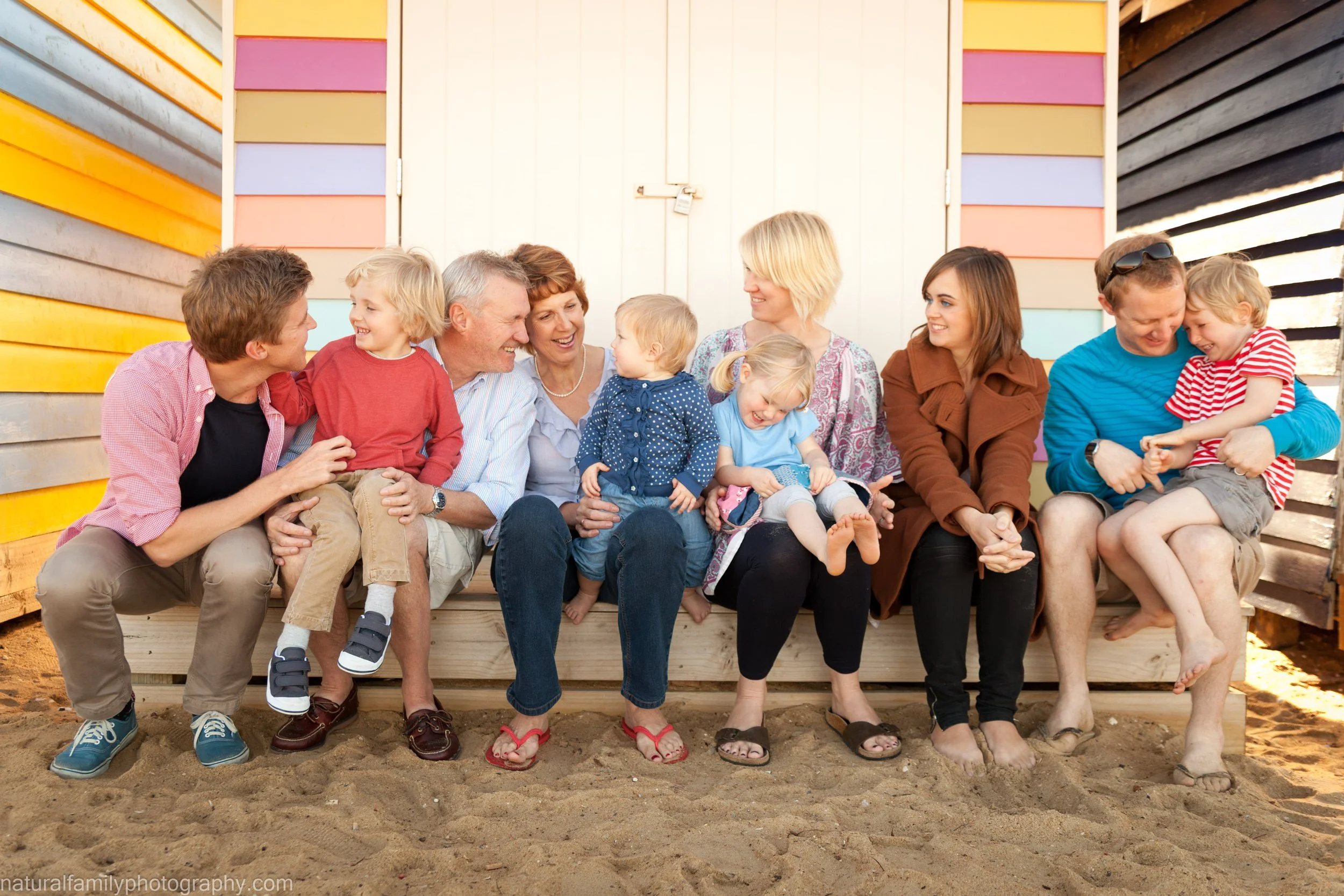 A large multigenerational family sitting on a wooden platform on the beach, smiling and interacting.