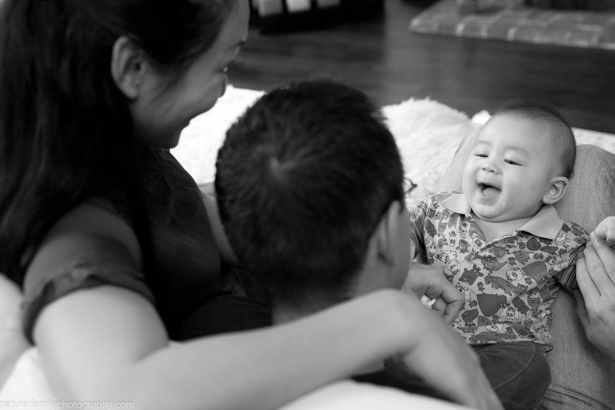 A joyful family moment with two adults and a baby, all interacting happily indoors.
