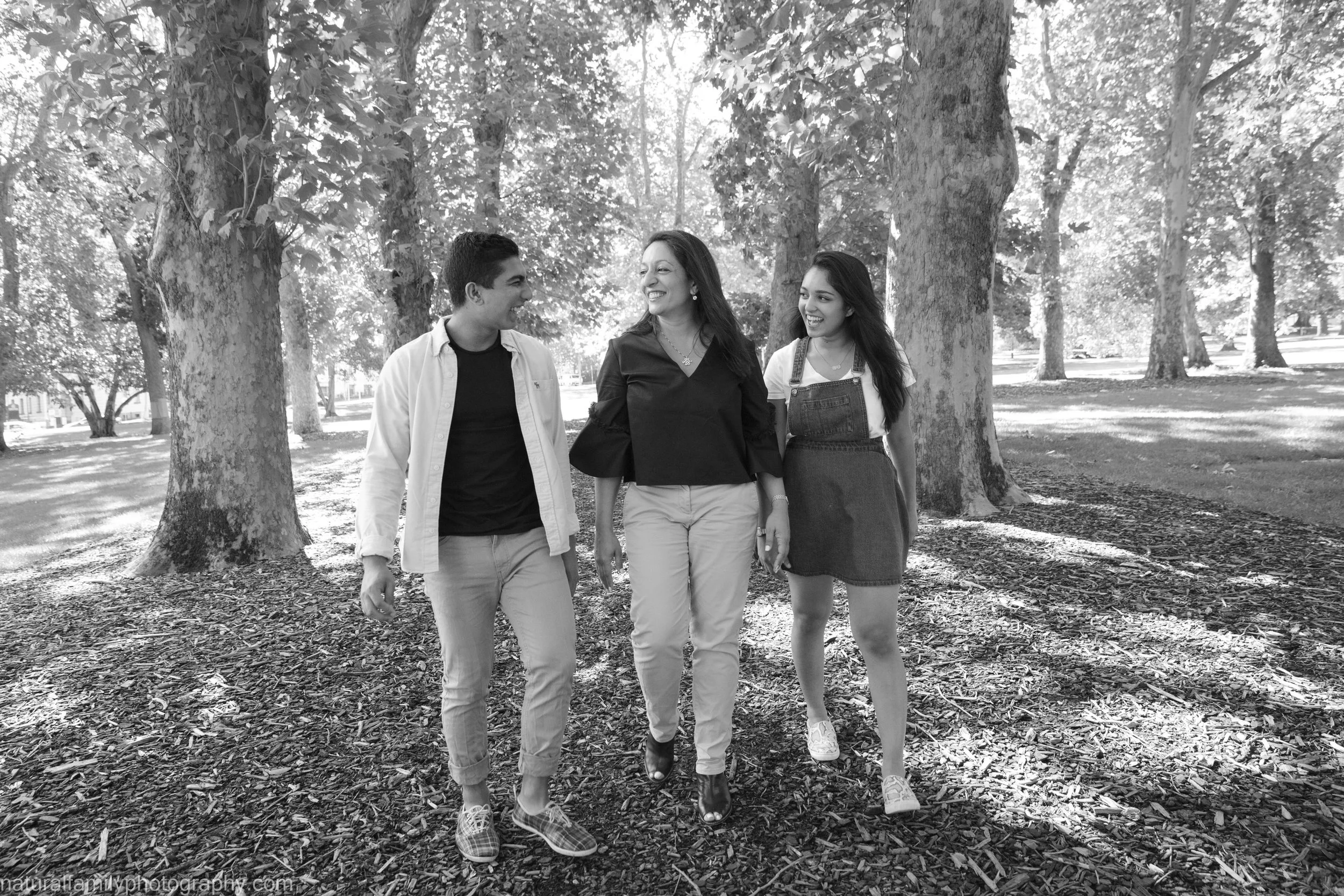 Three young people walking and talking in a park with tall trees in the background.