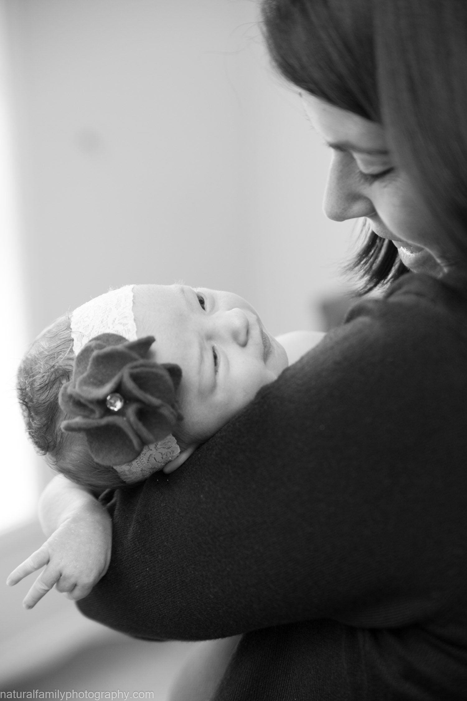 A woman holding a young girl, who has a bandage on her head and a floral headband, in an affectionate embrace. The girl is looking up at the woman with a gentle expression. The image is in black and white.