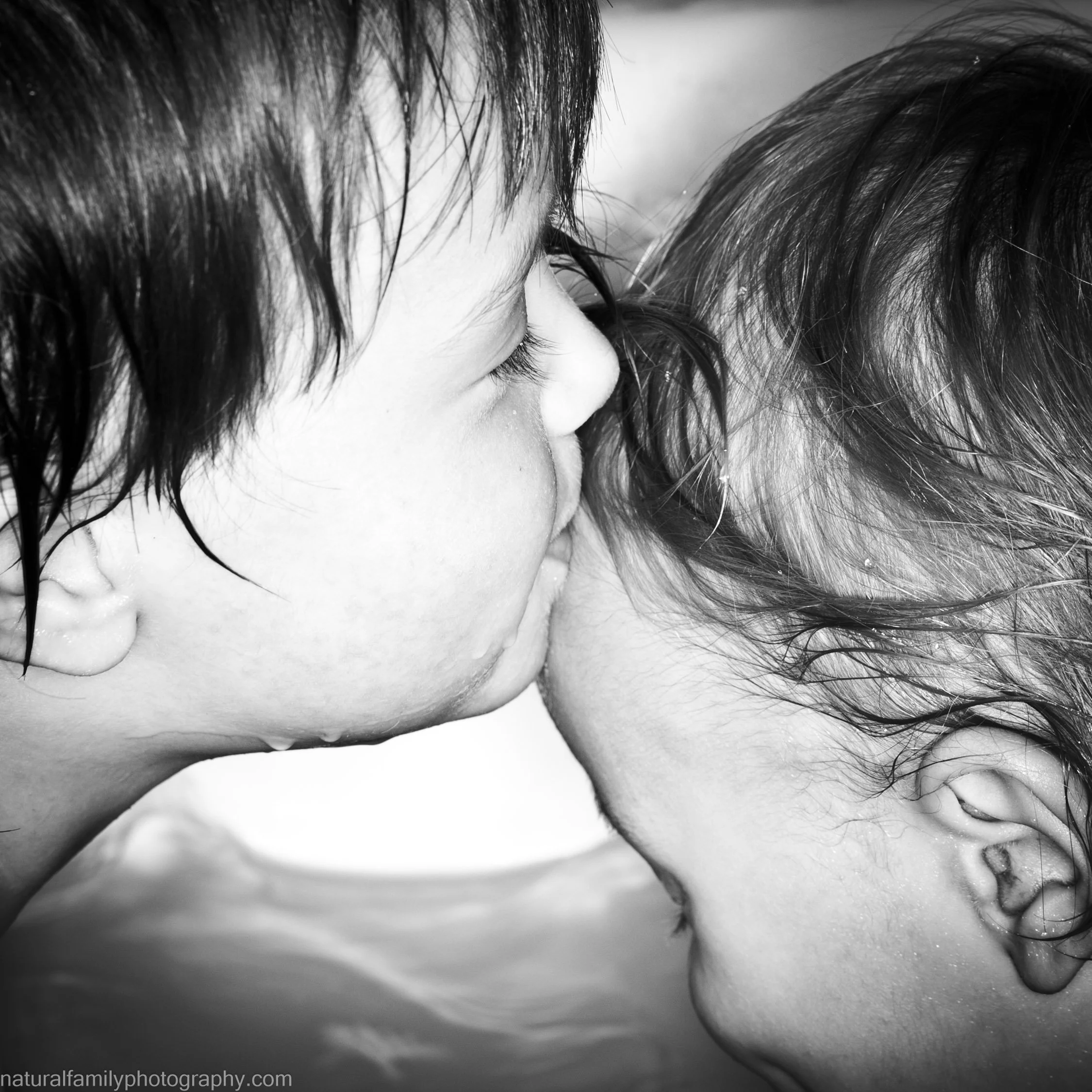 A black and white photo of two children with wet hair, kissing each other on the forehead. Loving family portraits by Natural Family Photography, Melbourne.