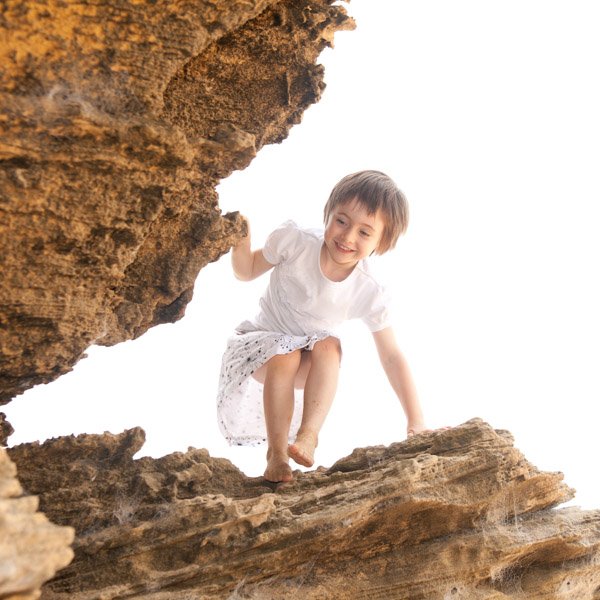 A young girl climbing on a large rock formation outdoors. Portraiture by Natural Family Photography, Melbourne.