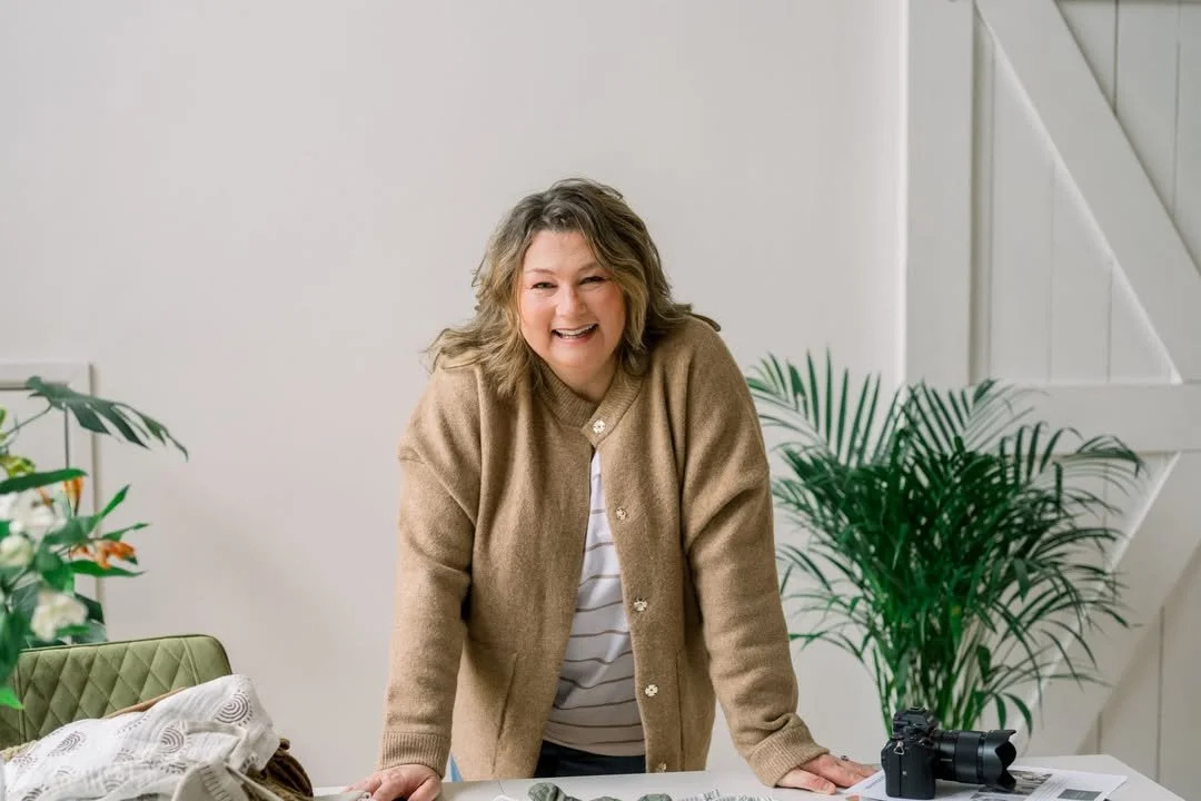 Robyn Sharman smiling standing behind a desk & next to a plant