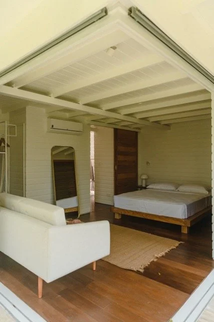 Bedroom with white bed, white couch, mirror, wooden wall, and air conditioner in a cozy room.