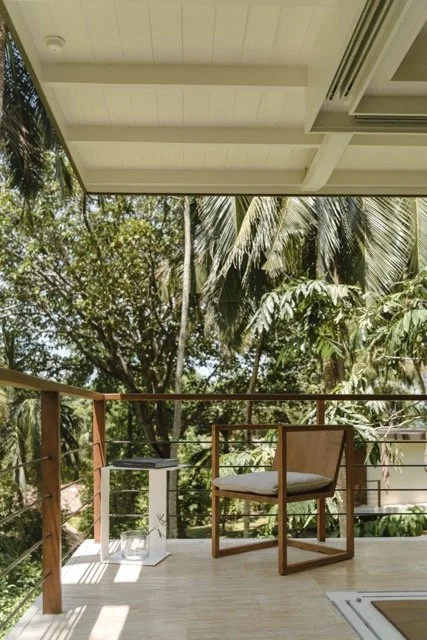 Balcony with wooden railing, outdoor chair, small side table, and lush green trees in the background under a white ceiling
