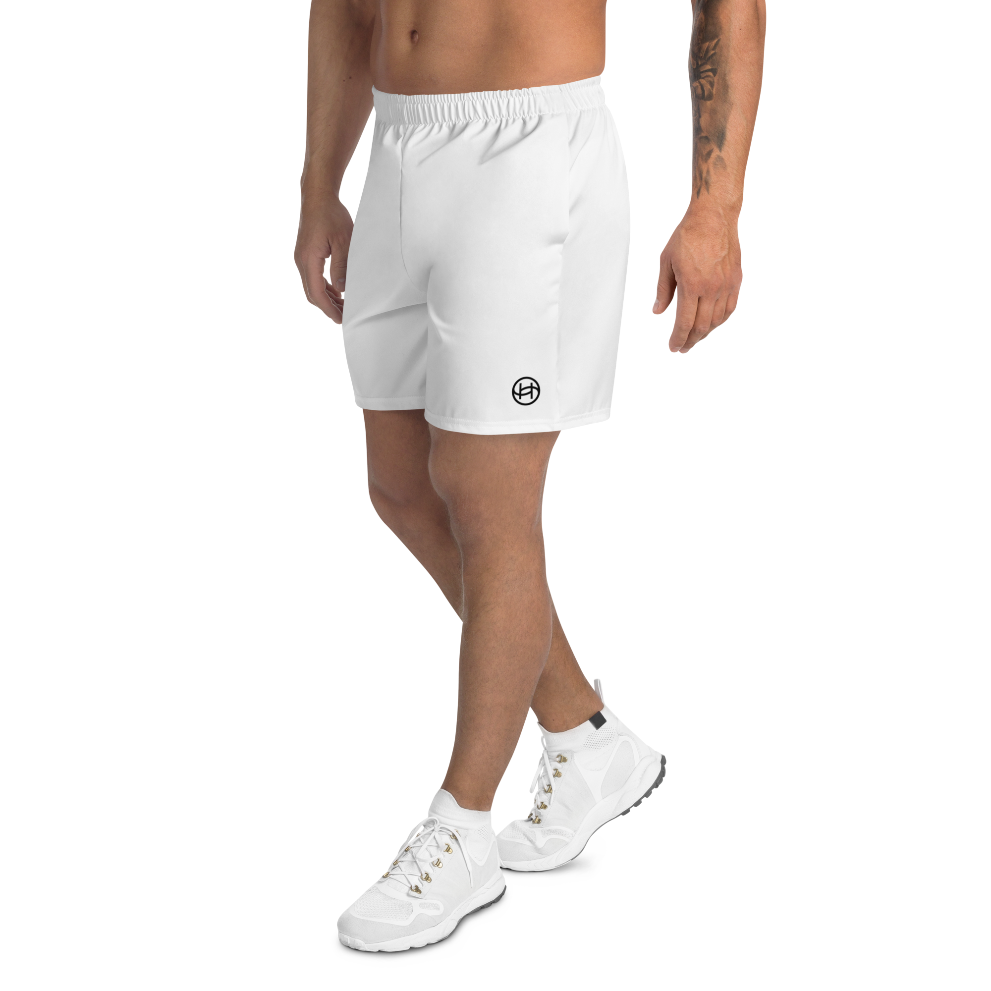 Male model wearing white athletic shorts with customizable logo, white sneakers, and a tattooed arm, standing with crossed legs against a white background.