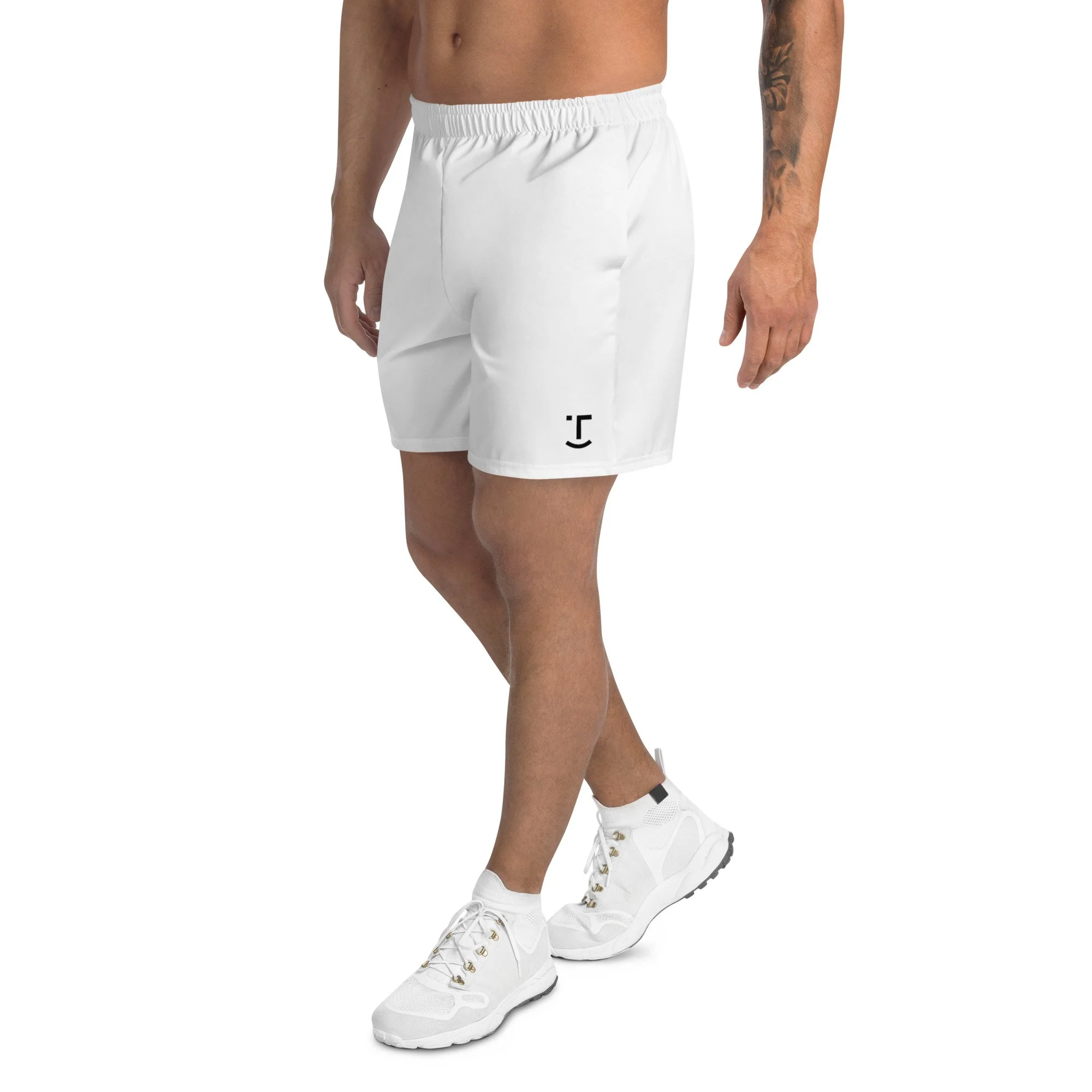 Male model wearing white athletic shorts with customizable logo, white sneakers, and a tattooed arm, standing with crossed legs against a white background.