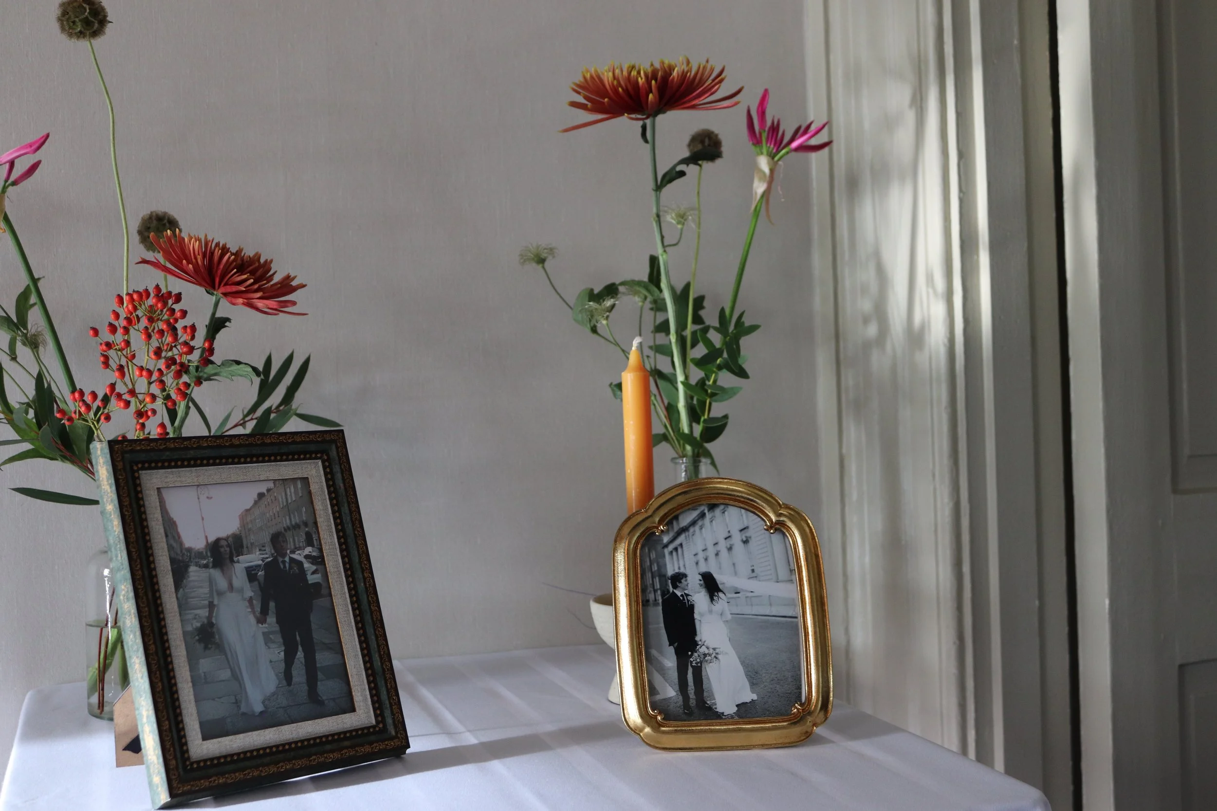 A table with two framed photographs of a couple, flowers in vases, and a candle.