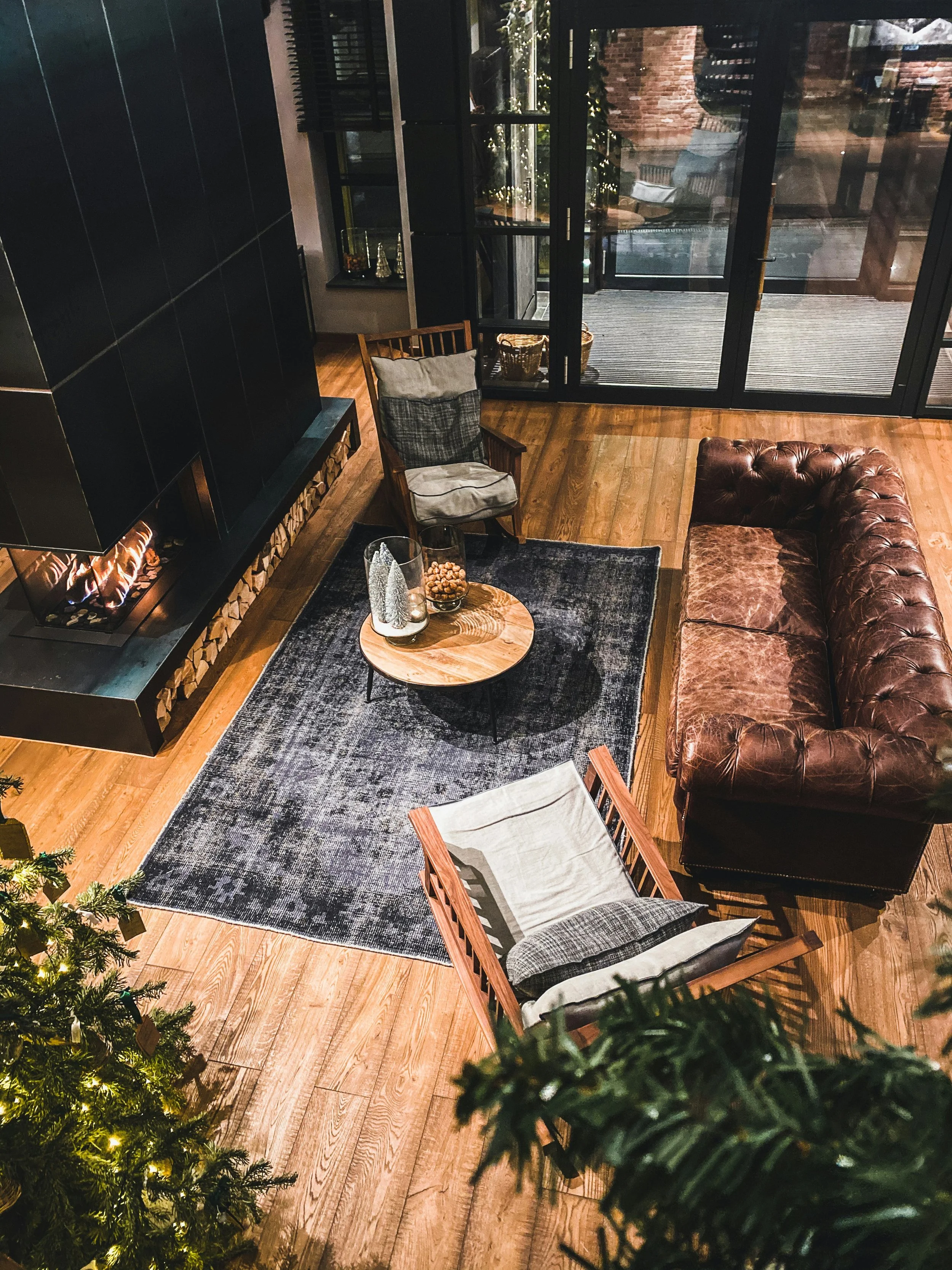 Cozy living room with leather couch, wooden chairs, fireplace, large rug, and Christmas tree