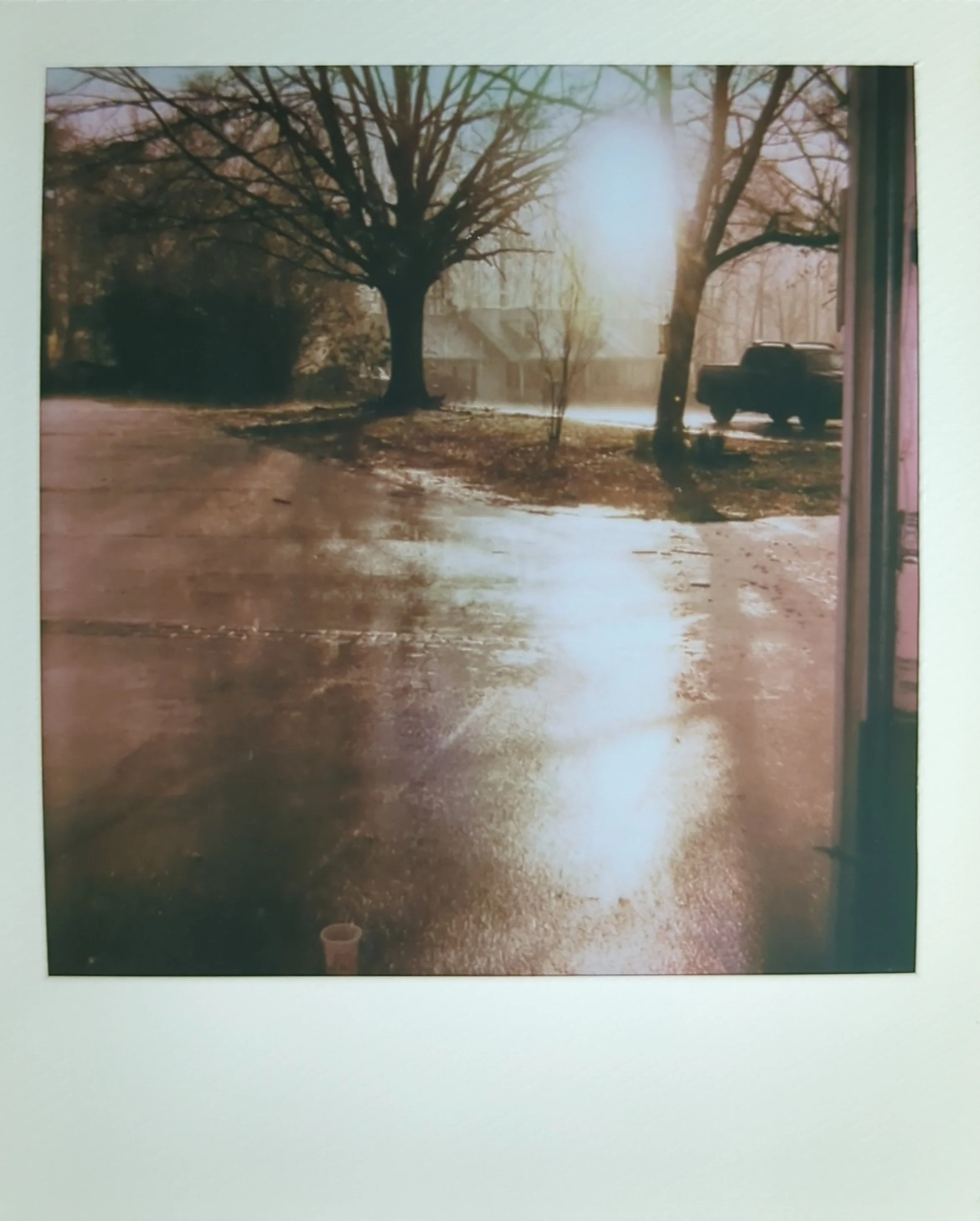 a polaroid photo of the sun shining through the clouds leaving a glow on a driveway on a rainy day