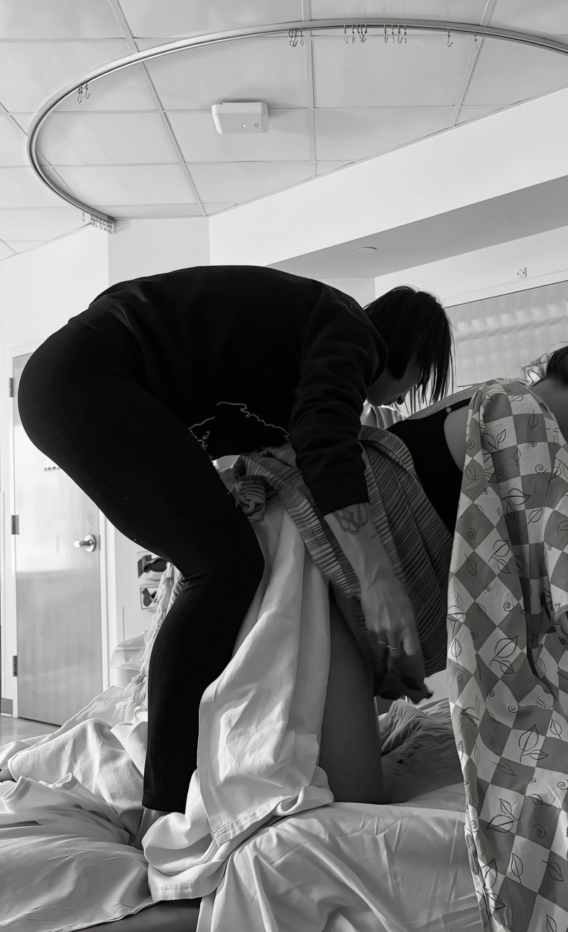 A doula assisting a person in labor on a hospital bed in a hospital room.
