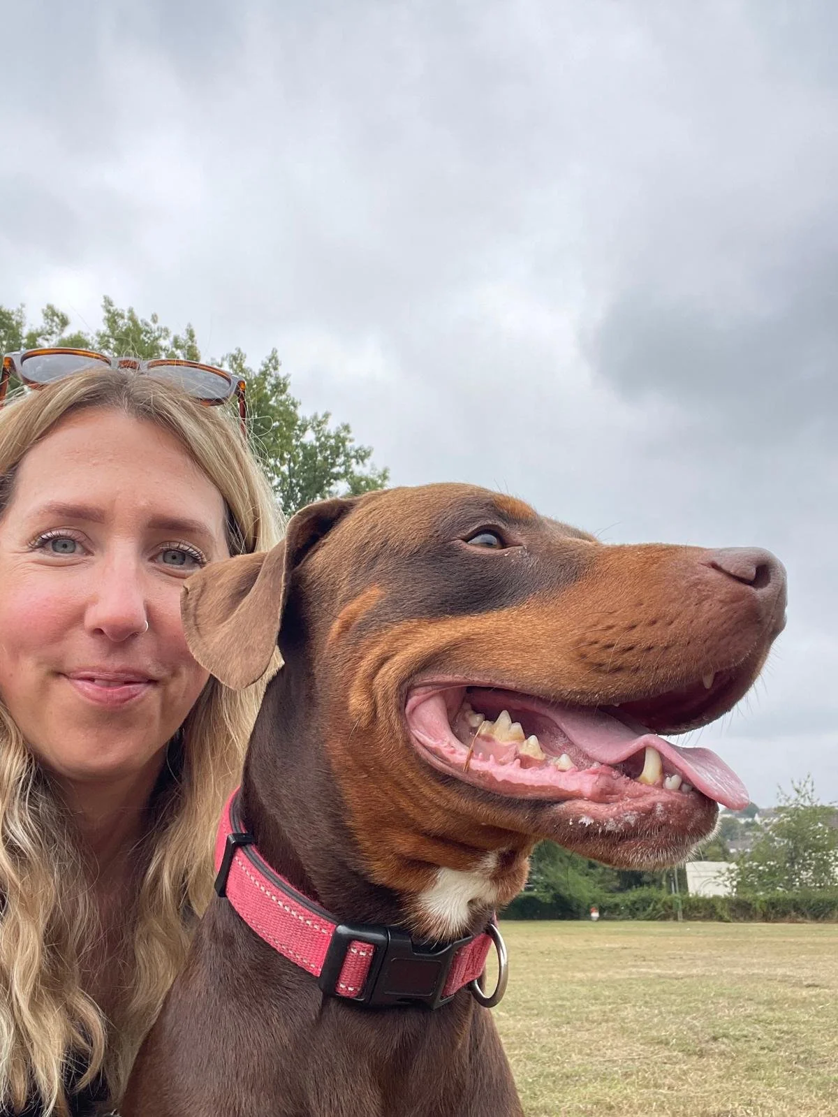 A woman taking a selfie with a large brown dog outdoors on a cloudy day.