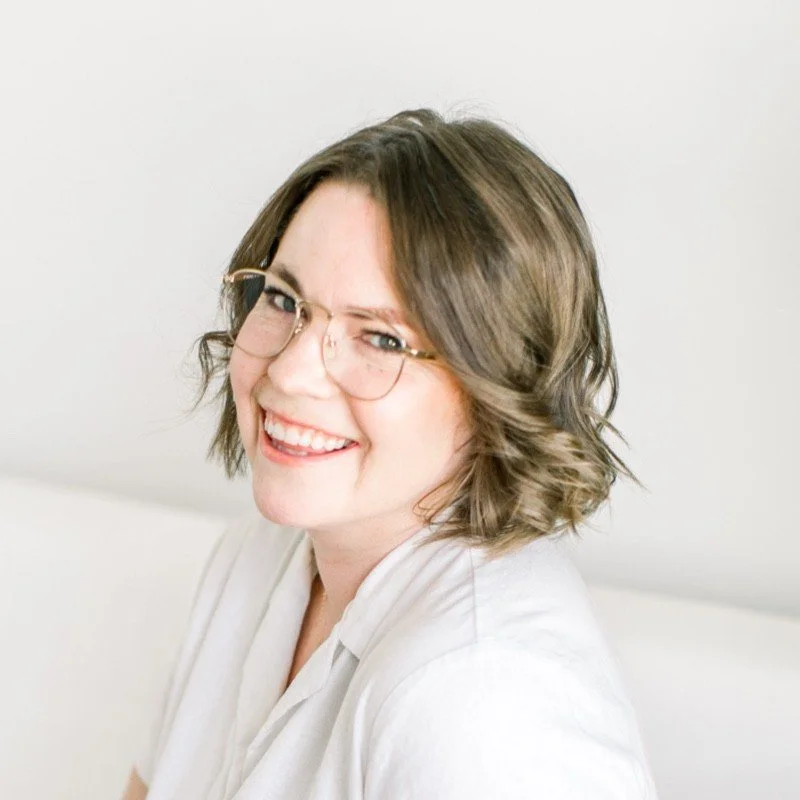 A woman with wavy brown hair and glasses smiling at the camera.