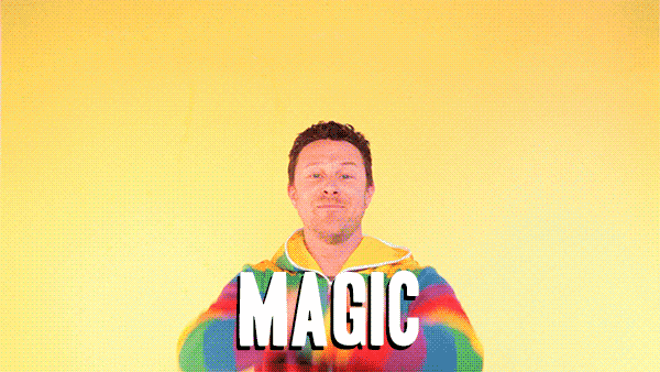 A man wearing a rainbow-striped hoodie standing against a yellow background with the word 'MAGIC' in large letters in front of him.