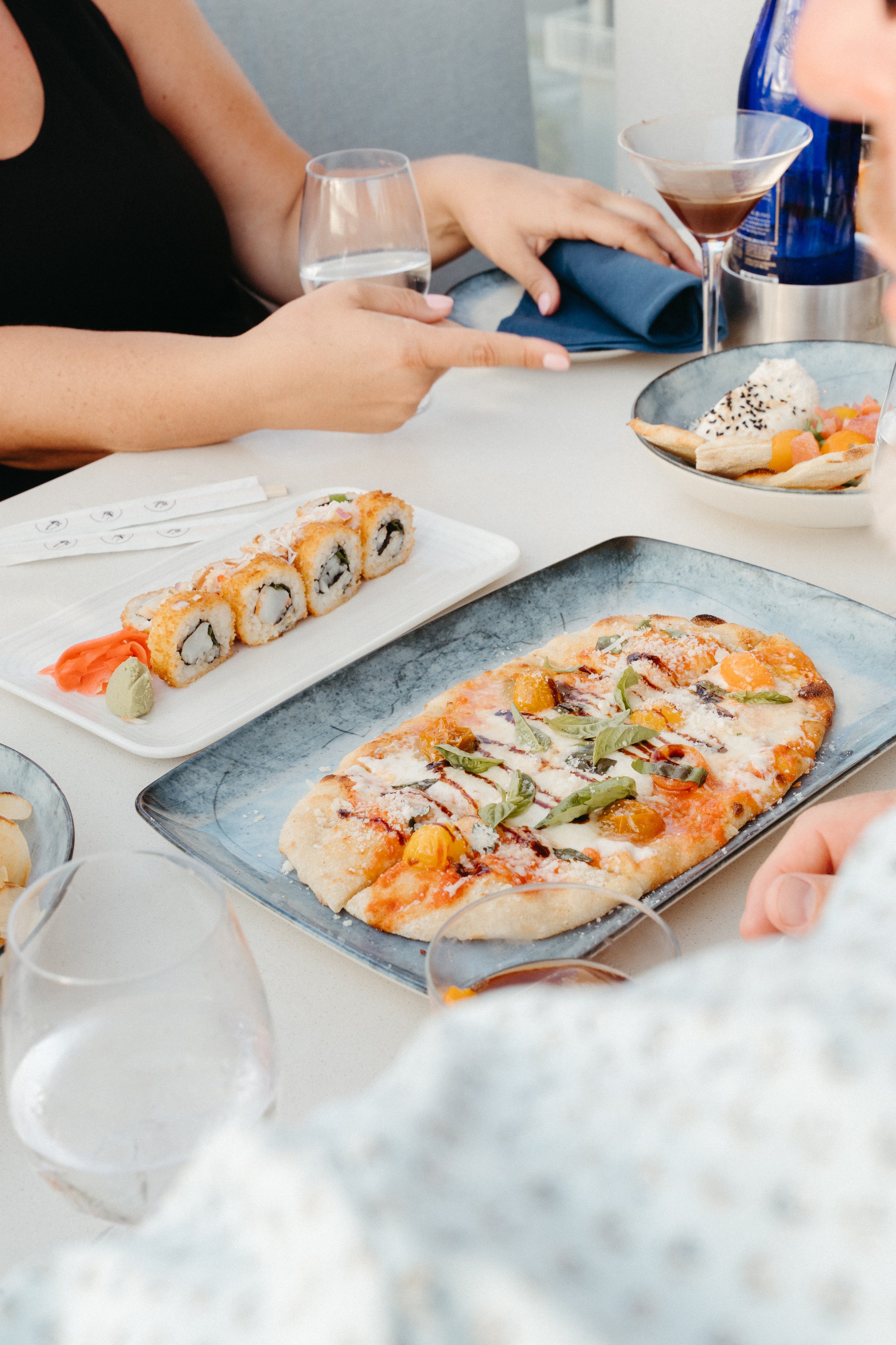 Sushi rolls, pizza, and various drinks on a dining table at Ocean Seven.