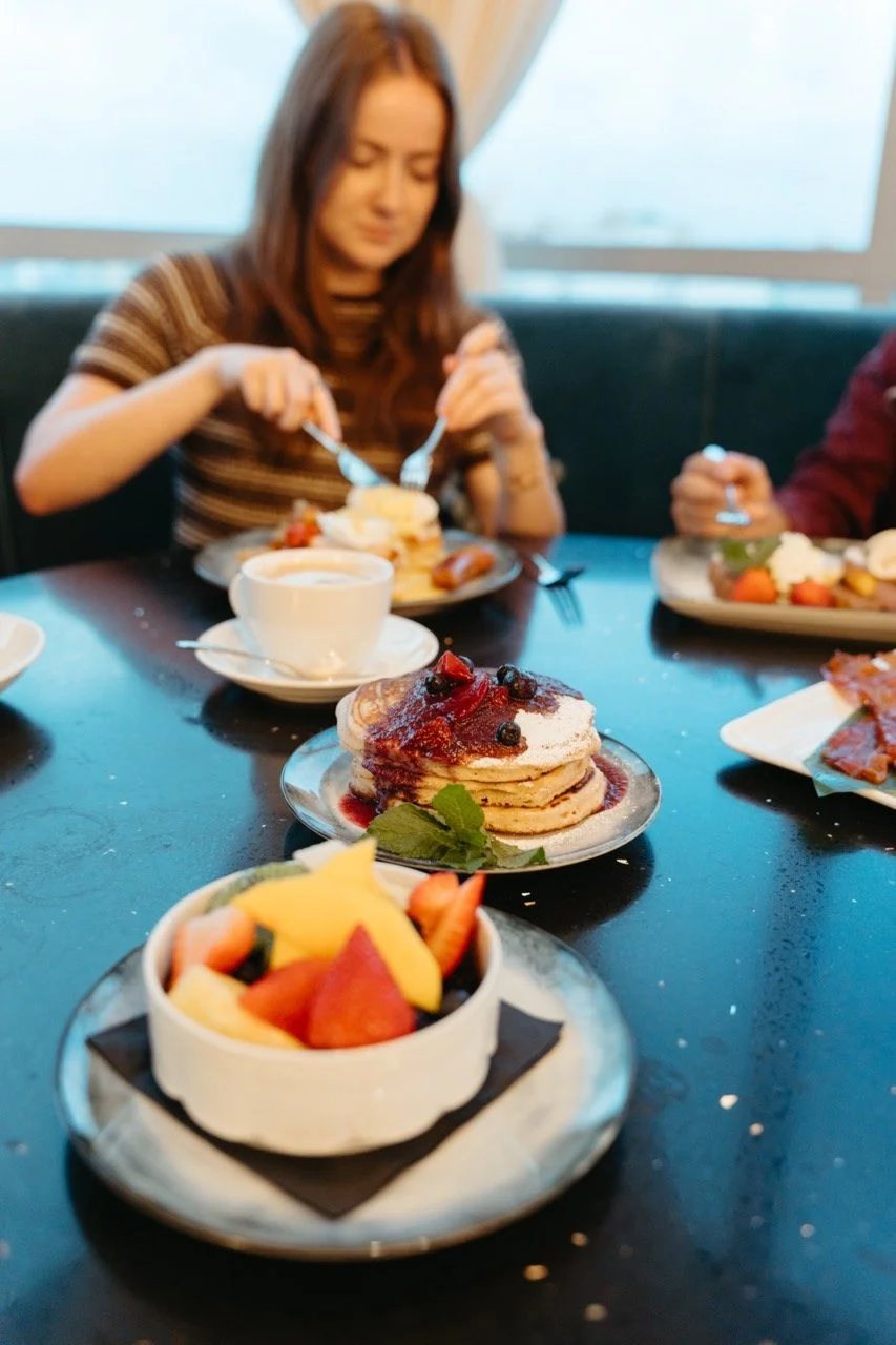 A table with various breakfast items including a stack of pancakes topped with berries and syrup, a fruit bowl, and a plate of french toast with strawberries.