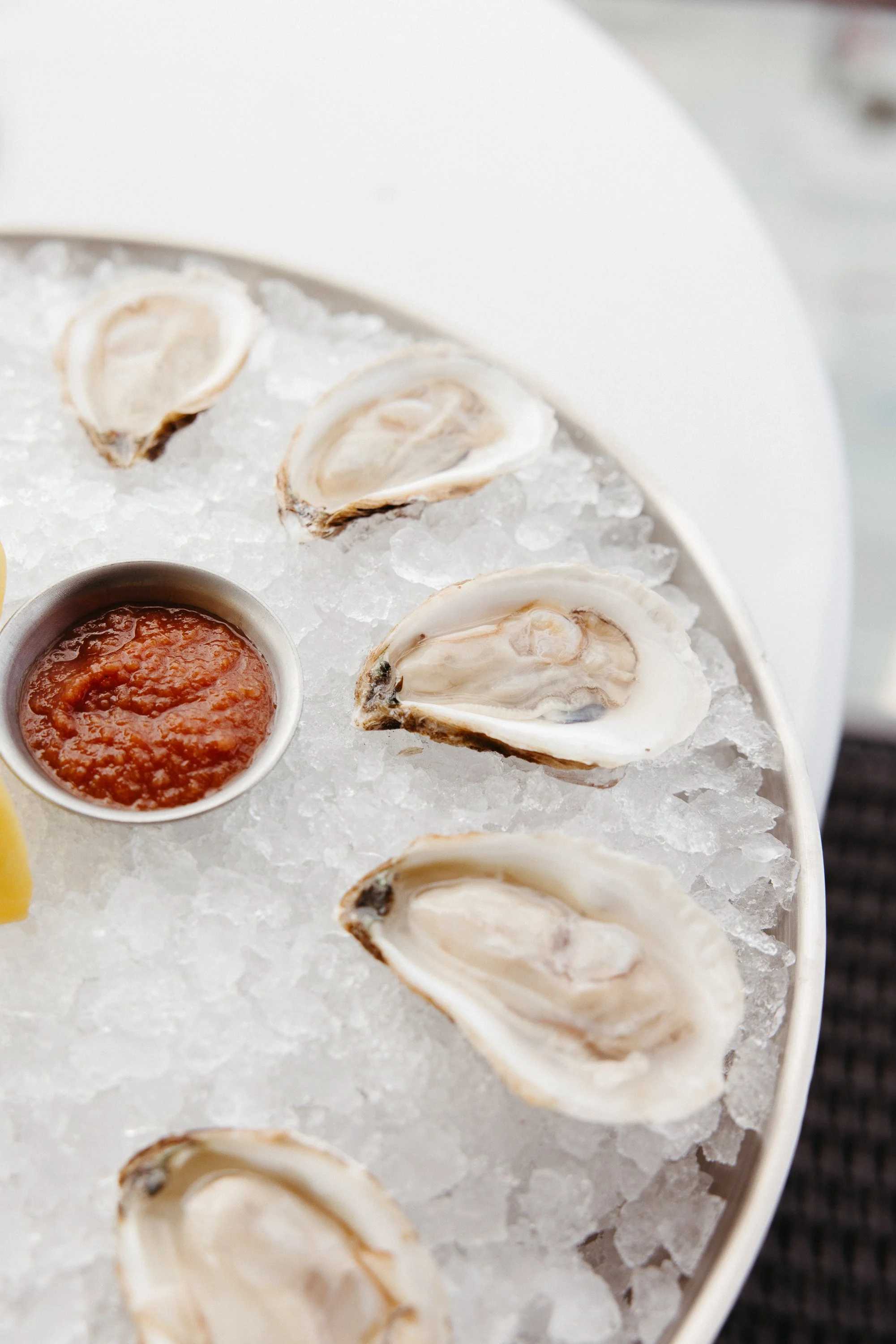 Close-up of fresh oysters on a bed of ice with a cup of cocktail sauce in the center.