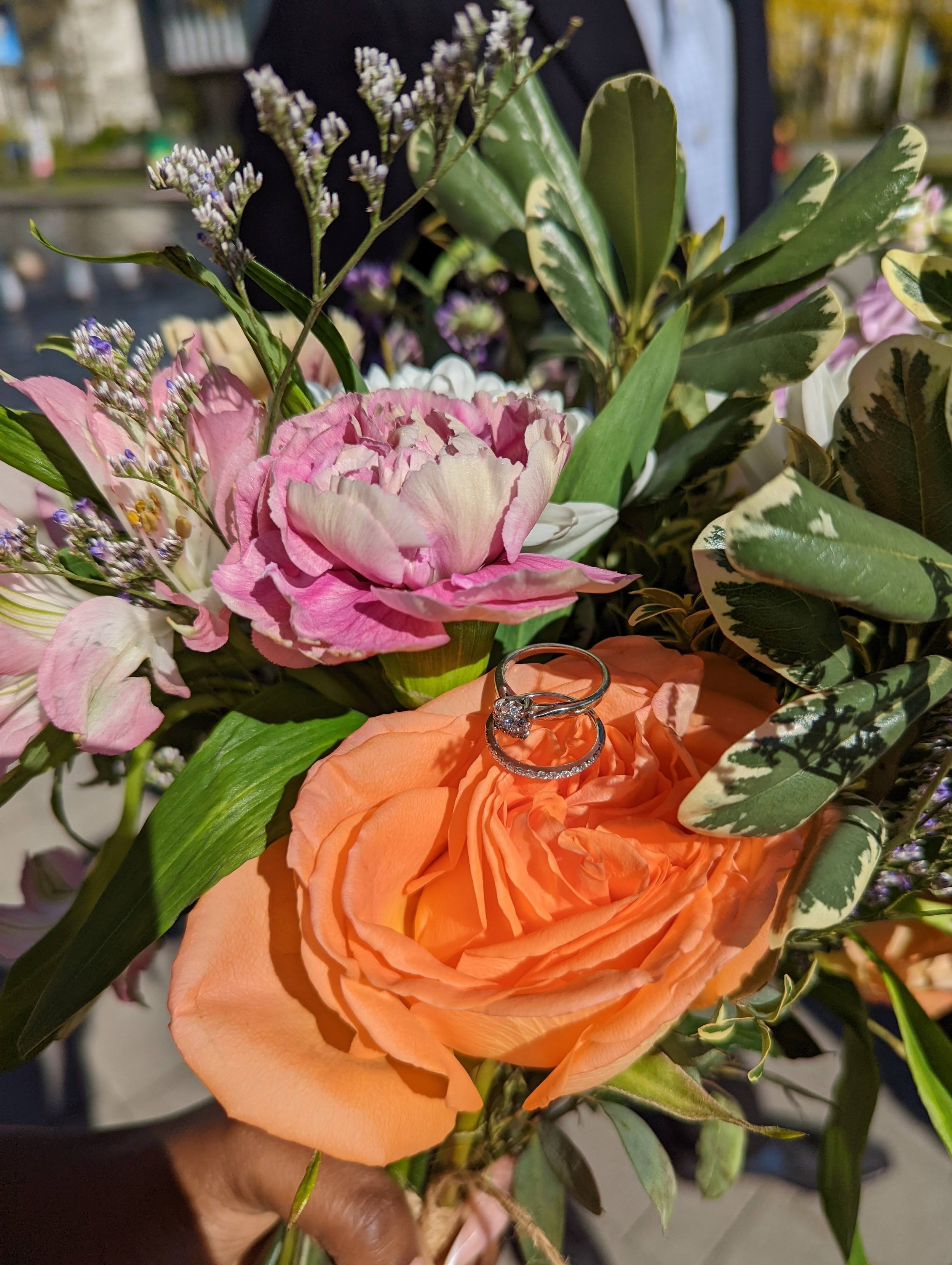 Ona Events wedding planning - a bouquet of colorful flowers, including pink and peach roses, with two engagement rings placed on the peach rose.