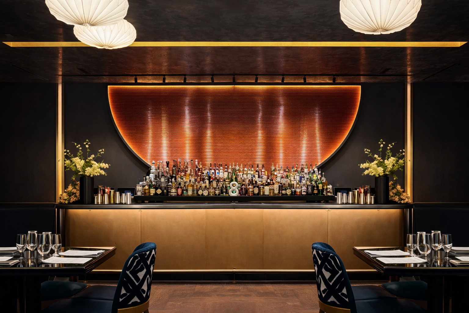 Elegant bar with a variety of liquor bottles, decorative flowers, and modern lighting, set in a stylish restaurant or lounge interior.