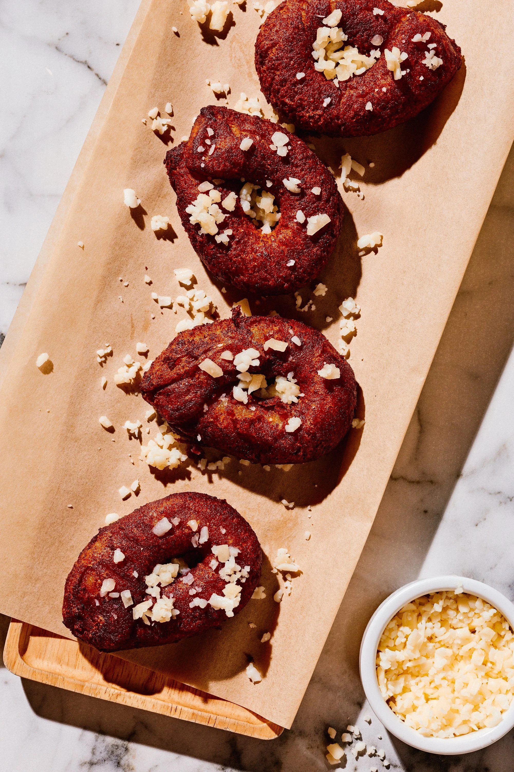 Cheese-filled Puerto Rican sorullos, deep-fried cornmeal snacks, topped with crumbled cheese on parchment paper.