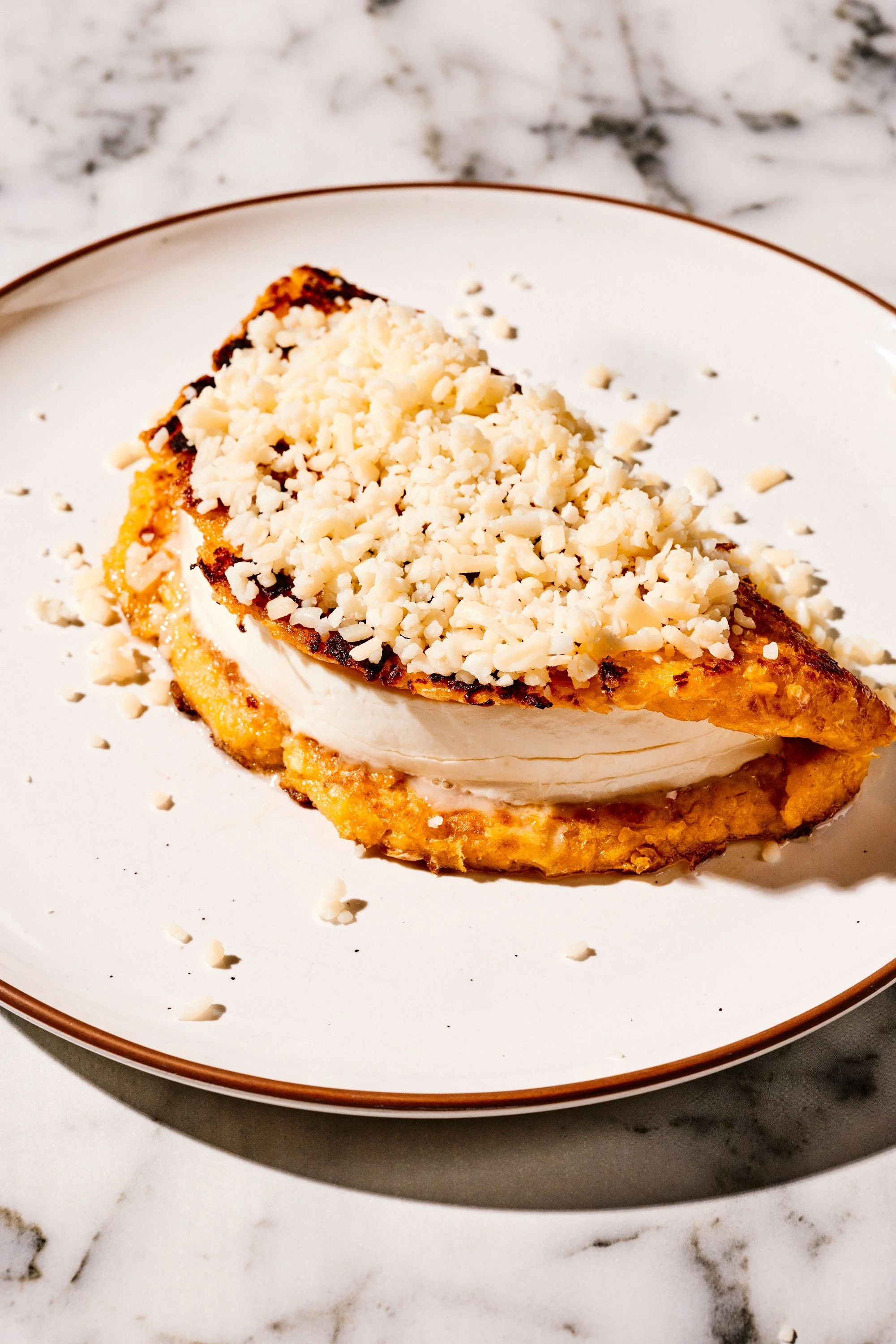 A Venezuelan arepa stuffed with cheese on a white plate with a marble background.