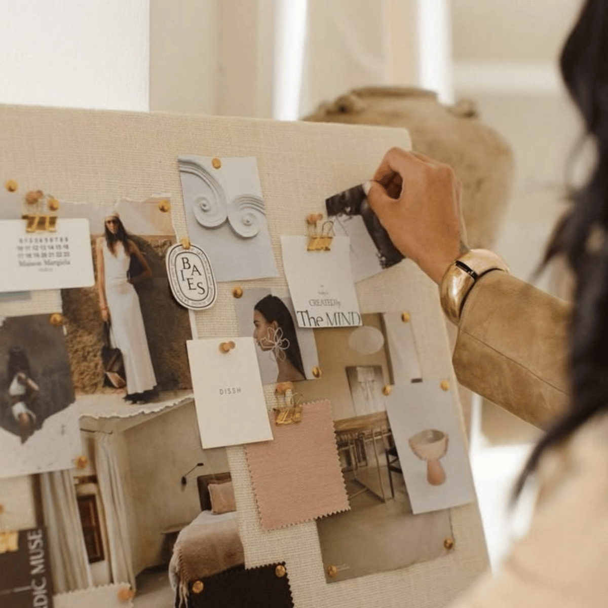 Person pinning a photo to a corkboard with various pictures, notes, and decorative items.