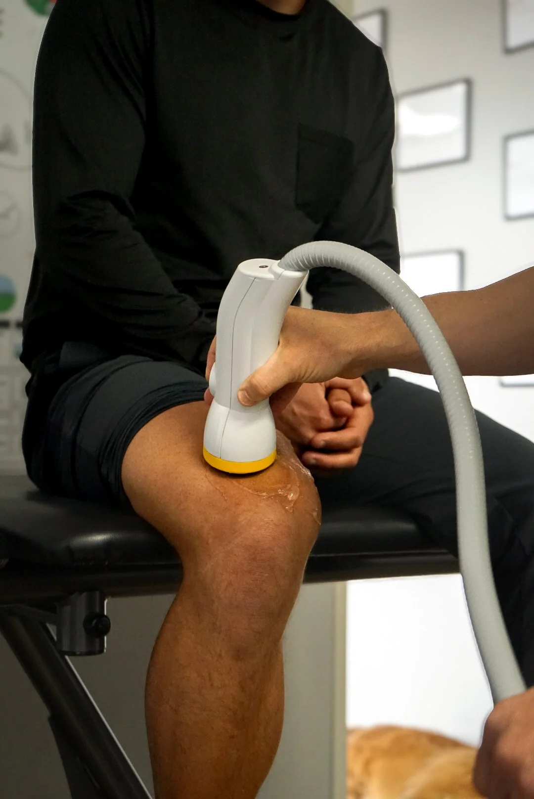 A patient receiving SoftWave Therapy on their knee with a handheld ultrasound device, while sitting on a chiropractic table