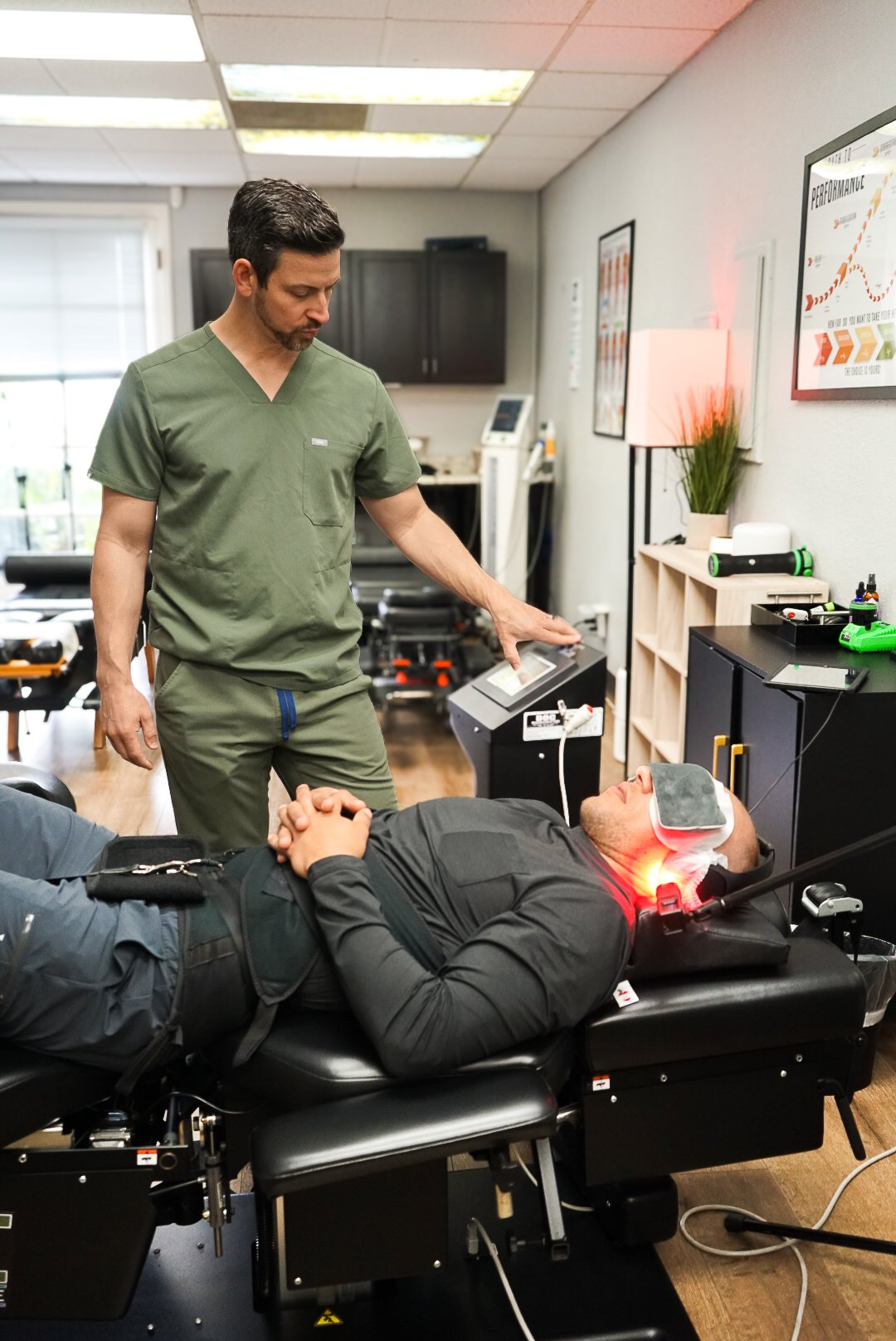 A man lying on a spinal decompression table low level laser therapy, while Dr. Harper in green scrubs monitors the decompression screen in the Calispine Functional Neurology clinic in Encinitas