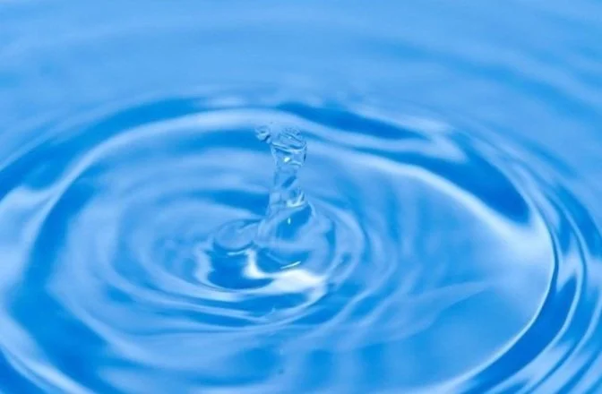 Water droplet creating ripples on a blue surface.