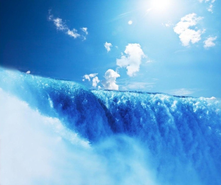 Waterfall under bright blue sky with clouds and sunlight.