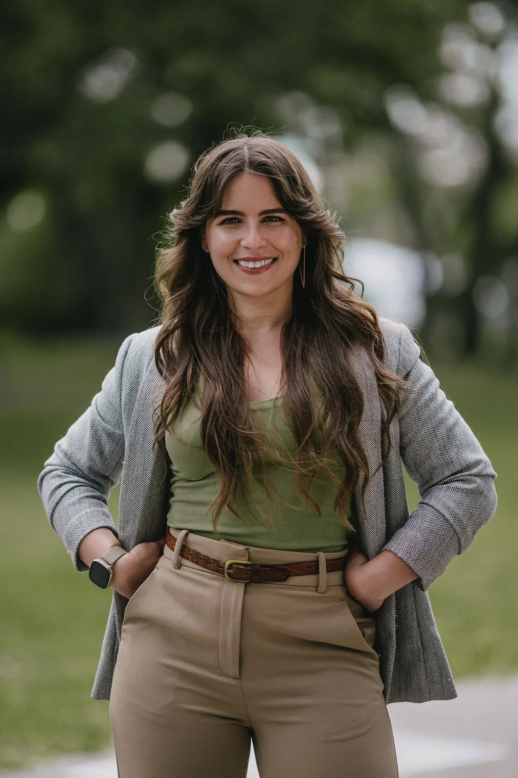 Smiling woman with long hair standing outdoors, wearing a gray blazer and green top.