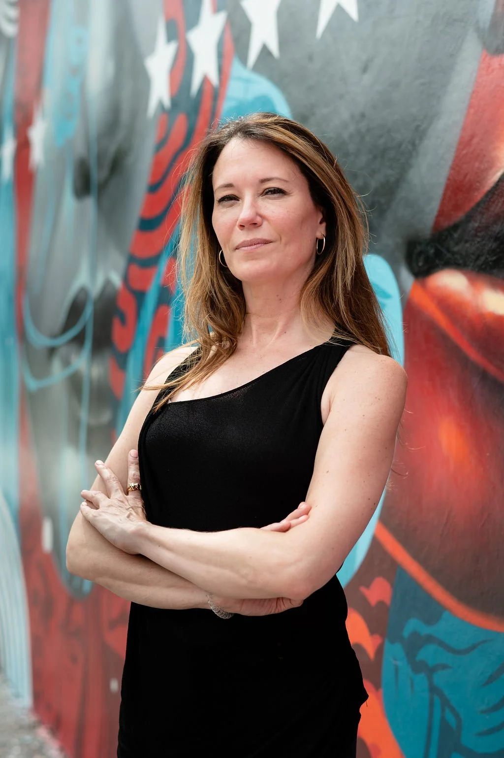 Woman in black sleeveless top standing in front of colorful graffiti wall with stars.