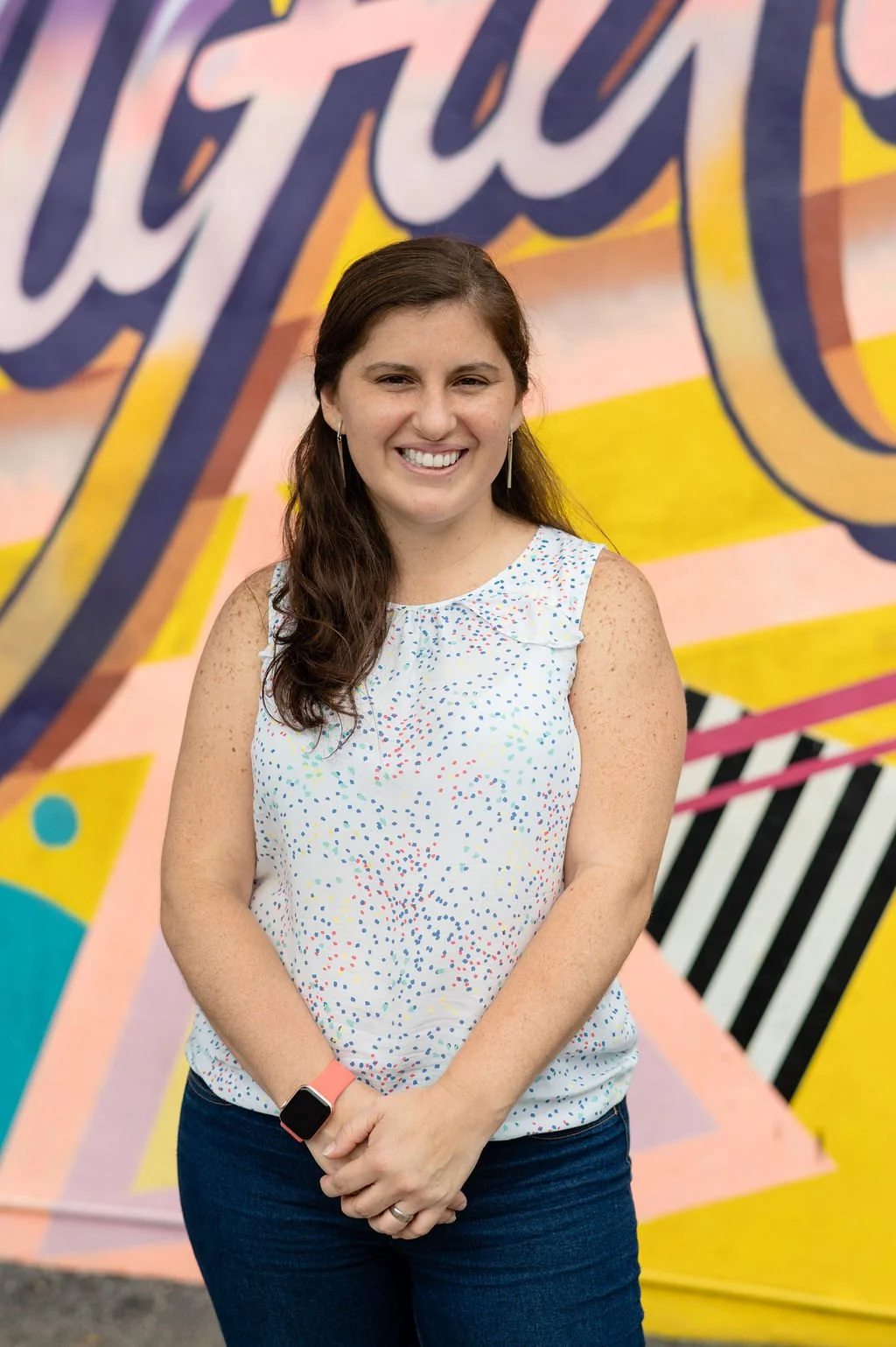 Woman smiling in front of colorful mural with abstract patterns and text
