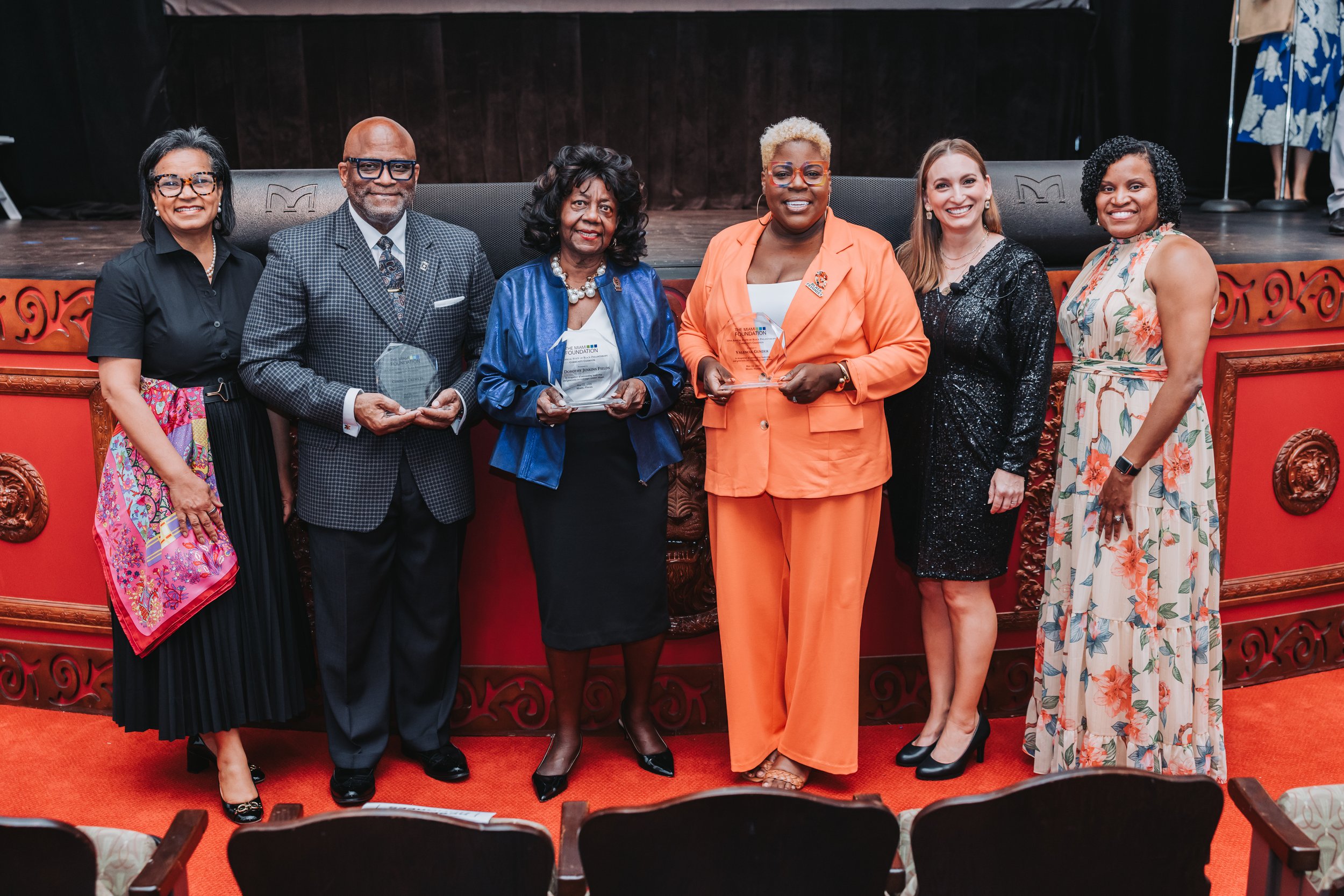 Six diverse individuals standing together on a stage, holding awards, at an award ceremony